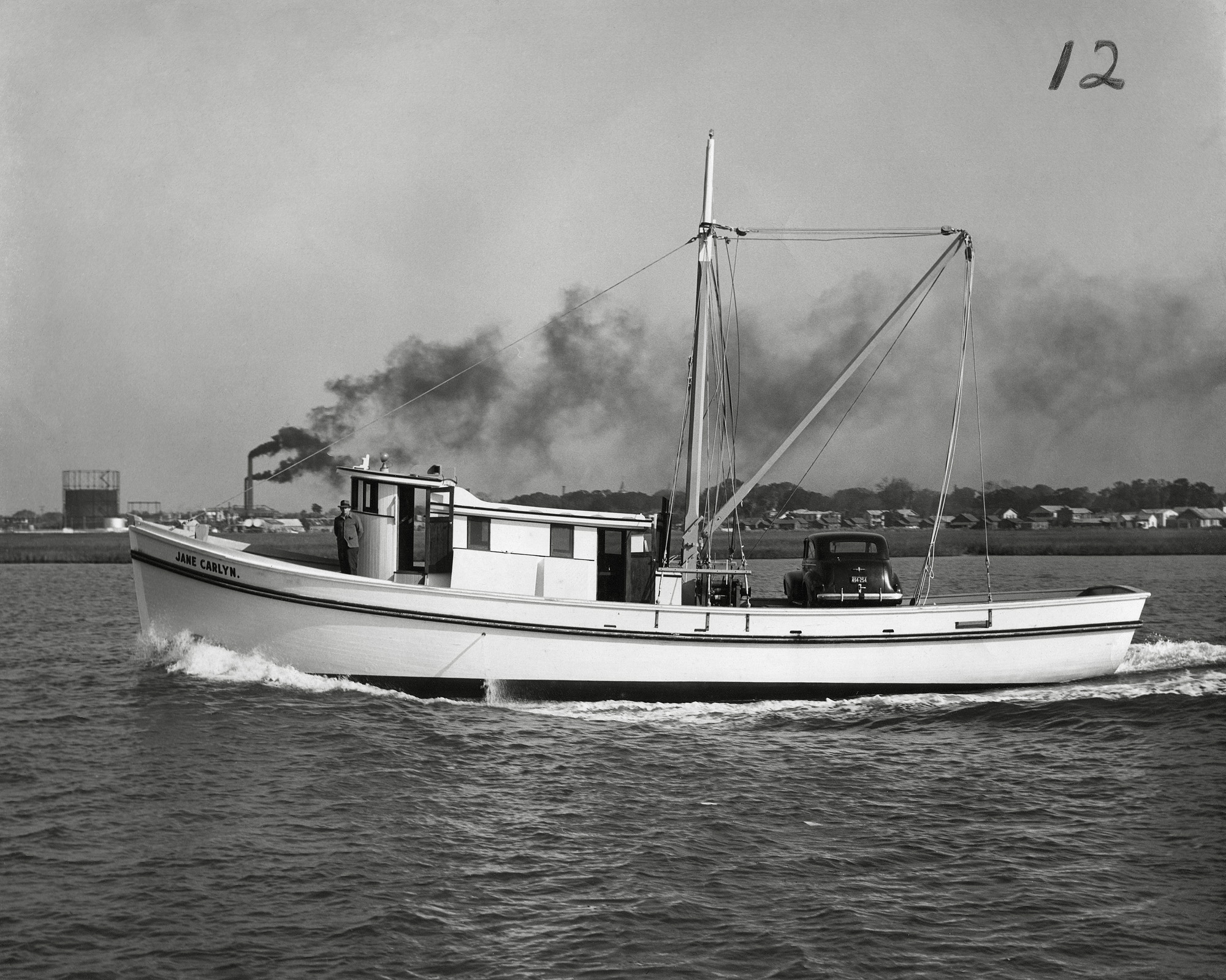 The 'Jane Carlyn' is shown here freshly launched and leaving the Diesel Engine Sales Co. docks in St. Augustine, Florida. Roland Styron stands at the bow of his brand new 65' wooden shrimp boat. Capt. Styron had a fish house in Hobucken, N.C. beside the R.O. Mayo fish house and later operated a fleet of shrimp boats that travelled as far south as the Florida Keys. Diesel Engine Sales Co. (DESCO) was a the leading builder of shrimp boats in the US and built 2272 wooden fishing vessels between 1943 and 1982. Photo taken in 1944. View full size.