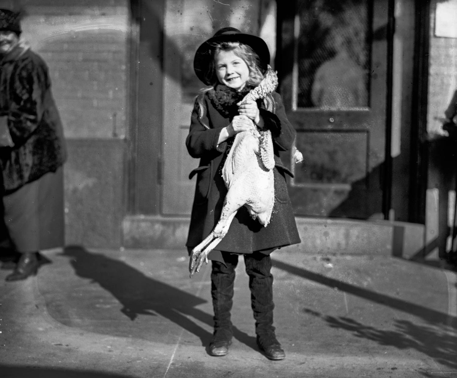 A young girl stands with her Thanksgiving dinner. From the National Photo Company collection, 1919. View full size.