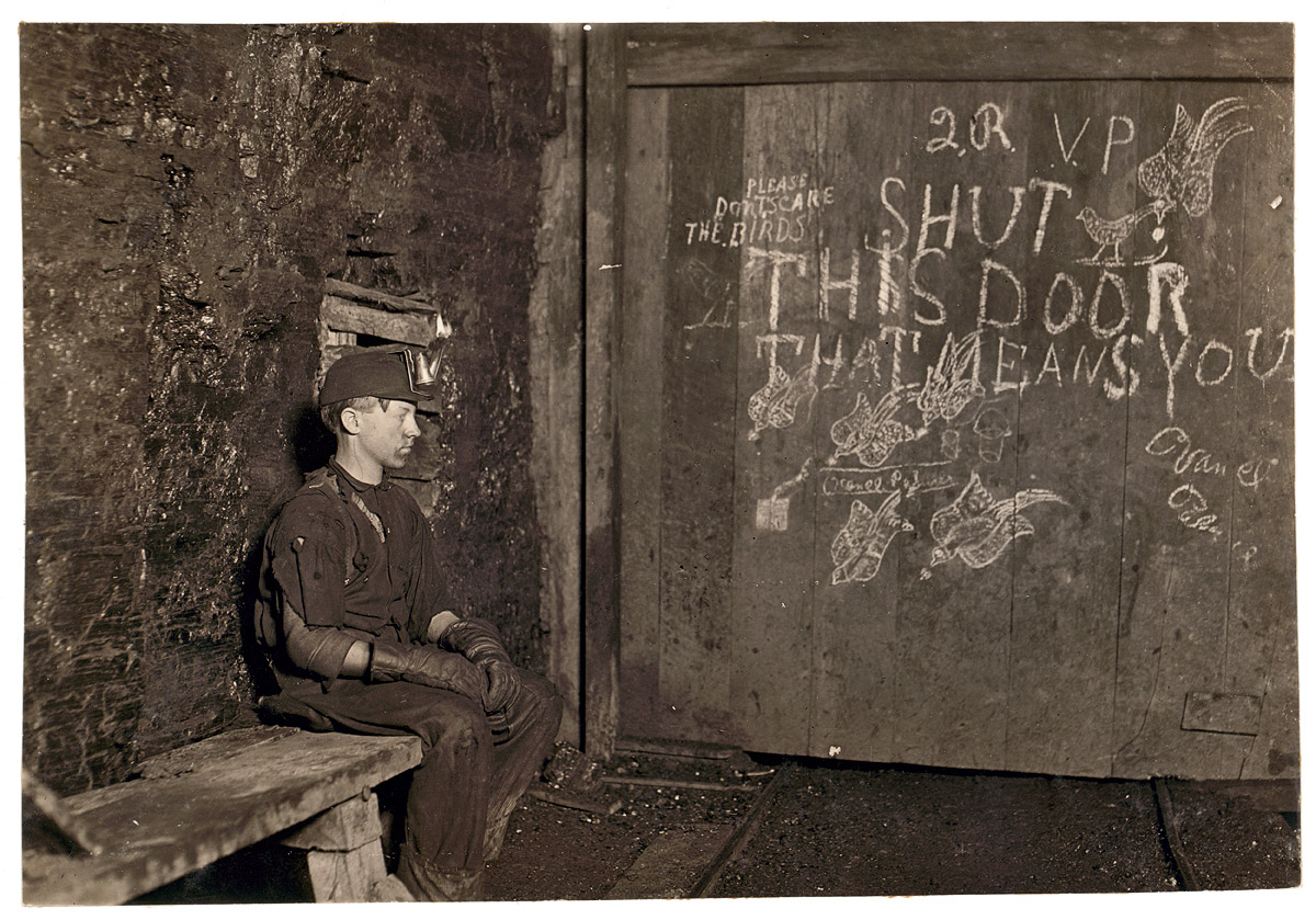 Vance, a trapper boy, 15 years old. Has trapped for several years in a West Virginia coal mine at 75 cents a day for 10 hours work. All he does is to open and shut this door: most of the time he sits here idle, waiting for the cars to come. On account of the intense darkness in the mine, the hieroglyphics on the door were not visible until plate was developed. September 1908. View full size. Photograph and caption by Lewis Wickes Hine.

One trapper's description of the job, which paid about $1.60 a day:

Trappers were responsible for opening and closing the underground ventilation doors. In those old mines, they had a system of doors between sections to direct the flow of air. Air was supposed to go up the main haulage and back to the fan. So a trapper sat all day by his door with an oil lamp on his cap. There was a "manhole" - a shelter hole in the wall by the track. The motorman would blink his light at me, and I'd throw the switch and open the door for him. Then, I'd jump into the manway until he was past, and run out and close the door. A trip would come along about every hour. Was I bored or lonely? Well, it was my job.