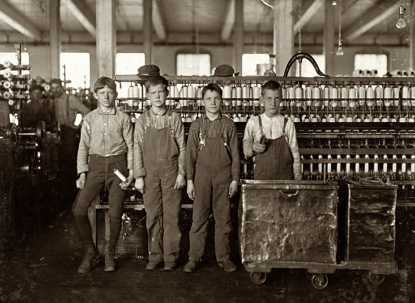 November 1908. Cotton mill workers at Daniel Manufacturing Co. in Lincolnton, North Carolina. Four doffers. Boy on left end (knee pants) said he had worked in the mills for seven years and some nights. At nights they work 12 hours, without any hour off for lunch. Eat when they can. Some of them "eat a-workin'." Photograph and caption by Lewis Wickes Hine. View full size.