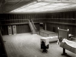 1910. "New York Public Library. A reading room." The NYPL on Fifth Avenue would open the following year. 8x10 glass negative, G.G. Bain. View full size.
EeriePerhaps the most powerful image I've seen for a long time.
Literary jailWhy do they put the books in jail? Is it to prevent theft? Could you just go pull a book off the shelf or would you need the librarian to get it for you?
DreamlikeEerie, like a dream of going to the library and is has no books. What is the large screen for?
[That's a signboard or directory with a glass cover. - Dave]
It pulls me in.I'm dying to slide down that banister, and then pull on my skates and have a turn around that big, empty floor.
Eerie is rightGrilles on the bookshelves. No visible electric lighting. A kind of desolate, dark atmosphere. Especially when compared of the library of Viipuri designed by Alvar Aalto. Too bad it was lost to Russia in WW2. Just Google "Viipurin kirjasto."
Book &#039;emGreat picture. Am I the only one who thinks this looks more like a prison? Alcatraz library comes to mind.
Reading Between the LionsThere are no books because the library was still under construction when this picture was taken in 1910. The new library opened on May 31, 1911. Still there, on Fifth Avenue, behind the Lions.
(The Gallery, G.G. Bain, NYC)
