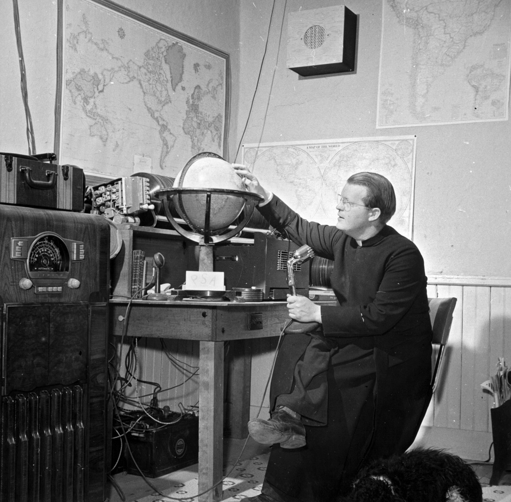 Father Smith broadcasting a news release in Spanish from his parish house broadcasting station in Questa, New Mexico. Photograph by John Collier, 1943. View full size.