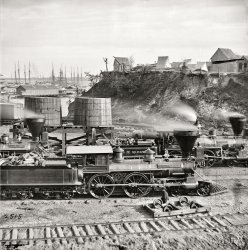 City Point, Virginia, circa 1865. "Gen. J.C. Robinson" and other locomotives of the U.S. Military Railroad. From views of the main Eastern theater of war, the siege of Petersburg, June 1864-April 1865. Wet plate glass negative. View full size.
Robinson ahead by a nose Seems that the Lt. Genl. Grant is running a close second. The named locomotives are from the Wm. Mason Machine Works in Taunton, Mass. The engine ahead of both seems unnamed. Might be an "American" locomotive or a Wm. Mason.
LocationThe terrain and the enormity of the facilities in place makes me almost certain that this was taken at City Point, Virginia, the Union's main supply depot for the area at the time.
[Another clue would be the first three words of the caption. - Dave]
Who&#039;s DrivingThe engineer is definitely not Buster Keaton.
Any ideawhat the black things are in the upper right hand portion of the picture?  When I looked at the blown up picture it looked a little bit like a lot of black socks hanging on a clothesline but that's obviously incorrect.
[It's a scratch in the emulsion. - Dave]
A bigger nameHard for me to see, but appears to be "Lt Gen. US Grant" on loco behind the Robinson machine. I am amazed at the hillside, ships and living conditions of the period.
Grant&#039;s Iron HorseSaturday we saw Grant's horse "Cincinnati;" today we see Grant's Iron Horse, "Lt. Genl. Grant," on the left.
Union IroncladA turret of a Union ironclad can be seen in the background over the top of the pier-side warehouse. This could be the USS Onondaga, which was stationed at City Point to prevent Confederate ironclads from breaking out of the James River and attacking the supply base. The problem is that the USS Onondaga had two turrets and I only see one.
Grant and Lee There is a photo so similar to this one in the book "Grant and Lee" by William A. Frassanito that it must have been taken about the same time.  It is in the City Point chapter view 8.  The tents and buildings on top of the bluff were part of the Railroad Hospital.  The wharf shown is a replacement for one that was blown up by saboteurs on August 9,1864.  The explosion killed 43 laborers and according to Mr. Frassanito narrowly missed General Grant who was in front of his headquarters tent at the time. His books have photos taken during the Civil War and then the same scene in modern times.
IroncladIn regard to the comment by Excel08 about the ironclad. Also according to Mr. Frassanito there would be about 200 vessels anchored off of City Point on any given day by the fall of 1864 including the ironclad ram "Atlanta" with one stack.
Poor LightingAmazing that all the headlights on these locomotives were a kerosene lamp in a box with a magnifying lens.
Spectre-visionNifty ghost in front of main tent!
Hillside erosionAttention troopers!
Gen. Grant has authorized the issuing of hazard pay due to the hillside erosion and the location of the outhouse.   
It is further recommended that only those soldiers who know how to swim should make use of the facilitiesafter dark.
Buster Isn&#039;t ThereI'll bet he is out visiting Annabelle Lee.
InterestingAlmost as interesting as the locomotives are the view of the ships in the harbor.
OopsHow did I not see that?  Boy, is that embarrassing.
Hey youget back to work.
25 years of progressIt amazes me to think that these beautifully turned out engines are only one generation away from the dawn of American railroading (think Tom Thumb and iron-plated wooden tracks). A person born in 1820 grew up with horse, foot or canal-boat travel, when 50 miles was a good day's journey. During their adult years, they saw the rise of well-established railroads that could travel fifty miles per hour. This, together with the telegraph, was the dawn of the "shrinking world."
The Third LocomotiveThe locomotive moving forward between the "Lt. Genl. Grant" and the "Genl. J.C. Robinson" is the "Governor Nye." This 4-4-0 was built by the Richard Norris &amp; Son locomotive works in Philadelphia, and was acquired new by the USMRR on February 18, 1863. Sent to North Carolina in 1865 to work on the USMRR, it was still in the USMRR inventory in April 1866. Another photo taken within minutes of this one shows it in the yard.

Watch that last step...I don't think that cliff-side staircase meets any imaginable safety regulation.
Bridge Of Beanpoples &amp; Cornstalks General J.C. Robinson  4-4-0 (Construction # 124) Formerly known as the USMRR locomotive General Haupt and acquired new by USMRR on January 17, 1863. Renamed General J.C. Robinson. Sold to the Baltimore &amp; Ohio Railroad in 1865.
http://www.nvcc.edu/home/csiegel/USMRR%20Locomotives.htm
"That Man Haupt has built a bridge over Potomac Creek, about 400 feet long and nearly 100 feet high, over which loaded trains are running every hour, and upon my word gentlemen, there is nothing in it but beanpoles and cornstalks."
Monitor identityThe monitor noted by others is most likely a Passaic-class ship and probably the Lehigh. The primary assumption is that the ship is perpendicular to the line of sight (as are the other ships). In that case comparing the monitor's funnel (tall thin light-colored tube to the left of the turret) to the turret, they are signifiicantly closer spaced than would be the funnel-turret distance for a Canonicus-class ship, the only other type which fits what is visible. This marks it as a Passaic. To identify it as the Lehigh is the stretch.  At least three Passaics were known to have been in the City Point area at this time; the Lehigh, Patapsco, and Sangamon. The Patapsco and Sangamon were both confusingly identified as having a white ring at the top of the turret/base of the rifle shield.  There is no ring visible on the turret of this monitor. The Lehigh was all black.
O Scale model Civil War model railroadBernie Kempenski is building a model railroad with these kinds of locomotives, etc.  His is dated 1862.  http://usmrr.blogspot.com  
(The Gallery, Civil War, Railroads)