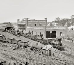 1864. "Nashville, Tennessee. Rail yard and depot with locomotives." Wet-plate glass negative by George N. Barnard. View full size. Another view here.
This Railroad Terminalis not eligible for the Good Housekeeping Seal of Approval.
Less is MoorishWhat bizarre architecture!  That sagging entry portal is being held up with that one flimsy pole? And the archways look Persian or Turkish or "Arabian" while the turrets look like an English castle.  The whole thing looks like it's going to fall apart any minute. I'm afraid Nashville here looks like Atlanta post Sherman!
Where&#039;s Buster?Great RR view...but I kept looking for Buster Keaton peeking out of one of the locomotive cabs, or sitting on a connecting rod kissing his girlfriend!
Perspective is an odd thingThose huge chunks of wood make the engines look tiny, even though I know they aren't. I also like the ghostly image of the now long-dead man in the shack. It's a rare treat to look back 100+ years into the past and I'm still amazed at the clarity of these old photographs.
Music CityThis shot was taken where the bulk of downtown Nashville now resides. You can see the state capital off to the right. Even today Nashville is a pretty small city. Growing up not far from there, it always amazed me that such a smallish city could have such clout in the world of country music.
NashvilleThe building that you see in the upper right hand corner of the photo is the state capital.  It was completed only a few years before the beginning of the war in 1861.  It still stands today.  
Nashville fell to Union forces without a fight in February of 1862.  However, in the fall of 1864, in a last ditch effort to relieve the pressure on General Lee's forces in Virginia, confederate president Jefferson Davis ordered  confederate General Hood to disengage from following Sherman to the sea and attack Nashville and after its capture move into Kentucky and then Ohio in hopes of the Union suing for peace.  So, on December 15th and 16th of 1864 Union forces came out of their dug in positions and attacked Hood who had over the two proceeding weeks dug in and waited for the Union forces of General Thomas. Then over those two days Union forces soundly defeated the confederate forces.       
WOW....What an incredible photo, and could be of great use to model railroaders doing that era.  The wood clutter would be almost impossible to manage due to the amount of engines and all burning wood....I guess there was no forest management in those days either.  As a Canadian I must ask what USMRR stands for.
CrenelatedThe "crenelated" appearance could easily be a Moorish or Spanish-Moorish influence. They weren't just "English castle" style but really pretty universal.
Telegraph linesThe timbers on the the crenelated corner towers (chimneys?) do look like rail ties, but they have been fitted with prong-like pieces of wood and ceramic insulators for telegraph lines. Some of the lines themselves can be seen running from the insulators on the front corner tower to the insulators on the scaffolding at the center back roof parapet, and to another timber with three insulators on the tower at the far back corner of the building. All of this looks like an ad hoc arrangement, perhaps the result of a wartime need for more telegraph lines than were needed for a peacetime rail depot, or to quickly replace lines that were downed when the brickwork was damaged.
Up thereOkay, I've got to ask.  What are those things sticking out of the "turrets"?
[They look like sections of track, complete with ties. - Dave]
Nashville DepotThis depot was on McLemore Street.  This Google view is pretty close.  Those might be the same bricks in the 1864 photo.  
View Larger Map
USMRR>> As a Canadian I must ask what USMRR stands for.
The answer can be found here.
CamouflageI looked at the full-size picture for quite a while before I realized that there are two workers sitting in front of the woodpile.
Pony truck journalsPlease note the external journals on the pony truck of the lead engine nearest the camera. That's something you did  not normally see on steam engines until the  the twentieth century and then not until the "twenties" and then it was unusual. C&amp;NW 4-8-4s had 'em. A few others too. Interesting! In 1864.    
USMRR   I am sure the meaning of USMRR means United States Military Rail Road. Rolling stock and engines were valuable for transportation during the Civil War. Far faster than horses capable of 40 to 50 MPH for long periods, the US government during this time depended on rail transportation. Nashville was a hub for the South plus it's Cumberland River traffic, hence the gathering of so much here.
Nashville Railroad Yard in 1864 by BernardThe State capitol building in the upper right orients you pretty well as to where Bernard took the Photo. Although the depot buildings are long gone, the RR yard is still there, although probably not for very long--the neighborhood is getting very posh now and CSX Railroad is sitting on valuable real estate.  
It is called the Kaine Avenue Yard and the rsilroad still uses it, mainly for trains passing through the city (the ones staying go on to the huge Radnor yards).  In the 1890's they built Union Station adjacent to the tracks--approximately where the lower right of the photo would be.  The center of the Yard lies just below the Demumbreun Street Bridge on Eleventh Avenue; Bernard probably took the photo a little ways up the hill, around Twelfth, likely across the street from where a strip club now exists. The photo was probably taken sometime around the battle of Nashville, but there are only a couple of shots of the Union battle lines and none of any action. Bernard preferred buildings to people.  FYI
(The Gallery, Civil War, Geo. Barnard, Nashville, Railroads)