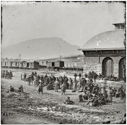 1864. "Chattanooga, Tenn. Confederate prisoners at railroad depot waiting to be sent north." Wet plate glass negative, photographer unknown. View full size.
Slim soldiersI noticed how thin all the soldiers are and also the woman and two children by the group of men on the tracks. I really enjoyed browsing over this picture since it showed so much detail.  
Train CarCheck out the train car that is labeled "Hospital Car."  I wonder what the interior looked like.
Officers and RationsBy their uniforms a number of these are officers. Their slimness derives from the poor rations most Confederates had in the last year of the war, so the Union rations must have been a relief. OTOH, they are may be en route to Block Island prison  on the Great Lakes, which  got miserably cold and dank in the winters.
RationsYes, the rations were lacking (I use that loosely) at that time of the War. I seem to recall a Confederate memoir by Sam Watkins recalling that the cavalry was eating the corn out of the feed that they were giving their horses.
Nice shot of Lookout Mountain in the background.
PrisonersSure they're skinny, so are their guards. But what surprised me is that most of them looked relaxed and kind of happy!
And that guy on the right, is he talking on his cellphone (above the tophat guy) (only kidding!)
Hospital TrainGiven the large opening in the center and lack of windows, this is a converted boxcar.  There were also purpose-built Hospital Cars that more closely resembled passenger coaches. In both cases, they were specially equipped for stretcher cases, however the boxcar's large center door opening would facilitate moving wounded in and out of the car. Period illustrations show a stove for heating, and what appears to be a double boiler for heating water or perhaps cooking at the opposite end of the coaches. As the boxcar shown here has two smokejacks on the roof, it appears it was similarly equipped. 
For some period artist's sketches and information on the cars, including an interior sketch circa 1864, click here.

RelaxedYeah, I'll bet they are relaxed!!  After being in battle off and on for a couple of years, they know they will have it better in a Union prison camp than in the Confederate Army.  Sure, the prison camps weren't a Hilton Hotel but at least you weren't getting shot at and shelled all the time.
Family HistoryOne of my relatives was captured in the fighting around Chattanooga near the end of 1863, probably several weeks before this picture was taken. He ended up at Rock Island, Illinois, from December 1863 to June 1865. 
The commenter who wrote, "the prison camps weren't a Hilton Hotel but at least you weren't getting shot at," may want to read up on Civil War prison camps. They were pretty horrific on both sides, and at Rock Island specifically, the prisoners had several months during which the guards on the wall made a habit of shooting prisoners at the smallest pretense or, whenever bored, firing off a random shot into the compound.
I certainly don't want to get into a discussion of which side's prison camps were "worse," because they were all pretty damn awful. It was bad, bad stuff, and don't think there were many prisoners on either side who would not gladly return to their regiments if they could.
All Union soldiersAll these men are Union troops. The overcoats that look gray are light blue. The photo is very remarkable in that it shows many different uniform styles and headgear.
(The Gallery, Civil War, Railroads)