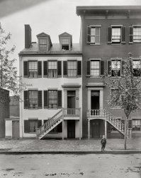 Circa 1900. "Mrs. Mary Surratt house at 604 H Street N.W., Washington." Boardinghouse owned by Mary Surratt where the Lincoln conspirators are said to have plotted the abduction of the President in 1865. Brady-Handy Photograph Collection glass negative, Library of Congress. View full size.
A watched totDon't overlook the people in the windows. The person on the right, bottom floor just behind the steps, seems to be taking a bite of something while in the house on the left, top floor dormer, he man may be holding a long pipe or a pen. The bits of daily life are what fascinate me about many of these pictures.
GuiltyMary Surratt was the first woman executed by the United States government, less than three months after the Lincoln assassination. Her death set off controversy that lasted over a century, but today there seems little doubt that she was closely involved in Booth's conspiracy. Ironically, her son John Surratt Jr. escaped the 1865 fury over Lincoln's death by fleeing the country; he was eventually captured and tried, but released after a mistrial and lived to be 72.
You want MSG with that?Surratt House has morphed into the "Wok N Roll" restaurant in D.C.'s Chinatown. There is a plaque.
View Larger Map
Mrs. SurrattAs she was lead up the gallows and positioned over the trap door, she kept pleading "Please, don't let me fall."
I've always wondered if she was referring to the height or the drop from the hangman's lever?
However she may have meant it, she fell. 
The StreetWere the roads paved in this era? When did widespread road paving begin in cities?
[The street in this photo is paved with asphalt. Asphalt paving in Washington and many other cities started in the 1870s. - Dave]
Pipe UpThe man in the dormer is smoking a "churchwarden" pipe.
Better in 1900The two buildings looked better in the 1900's than they do today. In the picture of the buildings today you can see where they took the stairs out and changed the entrances.  Looks pretty dumpy now.
I am surprised...that this building has not been acquired as a national historic treasure by the Government. Whether or not you sympathize with what Booth et al did in 1865 to President Lincoln and his Cabinet, this structure should be preserved and restored to its appearance in April 1865.
&quot;Chriswarish&quot;That photo looks like a Chris Ware illustration, including the boy!
Surratt House on the BlockThe Surratt House was added to the National Register of Historical Places in 2004.



Washington Post, Mar 24, 1922 


Lincoln Death-Plot
House Goes on Block
Surratt Home, Rich in HIstorical Past,
Fails to Bring Satisfactory Figure, However

A three-story brick house, once one of the proudest and most pretentious in the city, and rich in historical past, was placed on the auction block yesterday afternoon.  It was the home of Mrs. Mary Surratt, who was executed for her alleged share in the assassination of President Lincoln, and stands at 604 H street northwest.
A crowd of morbidly curious had gathered to watch the proceedings when the auctioneer unfurled his red flag and started to work.  There were a few bidders, but it took some time for the auctioneer to work the price up to any considerable figure.  The best offer received, $9.700, was considered too small, however, and the auctioneer announced that the house would be sold to a man who had privately offered $10,000.
The old house, recently painted a dark gray, seemed forlorn. The steps that many years ago had led to what is now called the second story had been removed, and the entrance was on the sidewalk.  Where the steps once led into the house, there was a door that had been closed many years.  In and out of it at one time had gone men and women whose deeds were to shake the foundations of the country.
Mrs. Surratt used the house for many years prior to 1865 as a boarding house.  It was in the little parlor on the second floor that the Lincoln conspirators met and planned the martyred President's death.  Mrs. Surratt was buried in Mt. Olivet cemetery, near the west fence.

My ancestral homeThanks for the great photo.  My great-grandma and her family lived in this house in the 1880s.  The story goes that they moved because of the nuisance of souvenir hunters coming by and trying to take a piece of the house.  Their next address was 606 H; so would this be the house next door I wonder?
+116Below is the same view from June of 2016.
Streets RenumberedSometime after 1880 the streets were renumbered. This house was originally 541 H Street  at the time of the assassination, and later became 604 H Street.
(The Gallery, D.C., Kids)