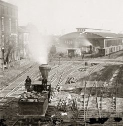 1864. "Atlanta, Georgia, railroad yards." Wet plate collodion glass negative, left half of stereograph pair, by George N. Barnard. View full size.
BurnedAnd on September 2nd 1864, the departing Union troops set fire to this railroad terminal and all its standing Confederate railroad rolling stock to ensure the enemy would not be able to readily reclaim the area. Next day, the mayor of Atlanta and aldermen surrendered the city to the Union, asking for further protections and no additional private property destruction.
That scenario was famously dramatized in Gone With the Wind, both book and film.
Point (Switch) BladesNotice how there are no blades as such. Sections of rail move across when the lever is pushed/pulled rather than the traditional machined tapered blade. 
BusterThis photo brightens the day by bringing Buster Keaton's "The General" to mind -- especially the scene involving the famous Keaton curve. 
Lil SwitcherCheck out the cute little switch engine steaming away over by the cut of cars on the right. Those stub switch stands are the precursors to the harp switch stands, seen here.
StacksDoes anyone know why the engine stacks are so big, especially compared to the size of the shunters. Creosote traps? Flash and ember traps?
Locomotive SmokestacksThe large stacks were indeed intended to help keep embers from falling on the grass along the tracks.  They are much more complicated than they appear since they had cast iron deflectors and screens inside the stacks.
Hangin&#039; OutThat's a lot of guys just hangin' out in the switchyard...
Link-and-pin couplersBefore the day of the automatic coupler, many a railroad worker lost limb or life to the dangers involved with building a train.
Blades, points, switchesThe "blades" you refer to are properly called "points."  Points move back and forth to be pushed close to the main running rails to make the locomotives go to the appropriate track. The switches are called stub switches.
(The Gallery, Atlanta, Civil War, Geo. Barnard, Railroads)