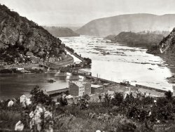 1865. "Harpers Ferry, West Virginia. View of Maryland Heights at confluence of Shenandoah and Potomac rivers." Wet plate glass negative (detail) by James Gardner. Civil War glass negative collection, Library of Congress. View full size.
Bridge and BoatThat bridge is lovely! And it looks like there's a boat being drawn by horses in the canal on the left.
Harpers FerryFirst saw a picture of Harpers Ferry in a 1950s National Geographic. Took the family to see it in 1958 and we climbed to the top of mountain where early pictures showed Union Troops. Now the National Park Service runs everything.
Maryland HeightsThis view looks downstream; the rocks on the far side are Maryland Heights. The bridge in the center is still represented by a line of piers adjacent to the present bridges.
Anniversary of the RaidNext year marks the 150th anniversary of the raid on Harpers Ferry. More info, including some very nice photos, here: http://www.harpersferryhistory.org/johnbrown/index.htm
Harpers FerryThey've done a lot of restoration in the town over the past few years.  It's always breezy because of the two rivers, so even on the hottest days it's usually pleasant.  Plenty to see and learn, and the restaurants provide rest and excellent provender!  Beautiful spot that we revisit often.
Harpers Ferry BridgeThe bridge spans are some of the earliest examples of the Bollman truss, a hybrid truss/suspension design which originated on the B&amp;O. The only surviving example is in Savage, Maryland.
Harpers Bridge Recent ViewsAnyone interested in "current" views?  1974 from very roughly same location:

and 12/6/07 opposite direction,

Bollman bridge piers remain in river at left, 1893 replacement bridge in center, 1930's replacement bridge at right as the railroad addressed the horrid original alignment here (look at those curves at span ends in the 1865 version).
The predecessors to the Bollman were blown up over and over again as the Civil War surged back and forth here. 
Harpers FerryAnd Amtrak can take you right there on the spot. There's the train station on the west side of the rivers, which provides a great view as well. Amtrak train the Cardinal from NY to Chicago through Washington DC will take you there. It's a beautiful trip through the Adirondack mountains going west, been through there myself more than once.  
Harpers Ferry TodayThe C&amp;O Canal Towpath, a national park, follows the Potomac River from Cumberland, Maryland, to Georgetown (D.C.). That makes it a 185-mile park, and the stretch through Harpers Ferry is among the most beautiful parts. Strongly recommended for anyone who can walk, bicycle or roll for a mile or two.
[There's also a nice footpath through the woods to Maryland Heights -- the top of the cliff to the left. The view is spectacular. - Dave]
One of my favorite places on Earth!I can remember stopping there on my way back to live in Kansas after graduating from high school and college in Maryland. I foolishly stood in the middle of the street and stared across the river at the tunnel.  A horn honked and I turned and saw a beautiful long-haired blonde driving a huge red convertible. The world seemed rife with possiblities at that moment in a way that was different from anything that followed in later years!
Harpers Ferry by TrainIt's the Amtrak Capital Limited, train No. 29 west, and 30 east.  Of course before Amtrak this town was served by the Baltimore and Ohio Railroad, and the original Capital Limited.
That House!!Having visited Harper's Ferry several times, I started to search my photos to see if I had a modern comparable shot... but the thing that stood out most to me was that tiny white house on the left edge of the photo!! The structure is still there and people always stop to explore it!


There's also an old ad that seems to be painted into the side of the mountain, which I've never been able to figure out what it says... I see "powder"...

Last Trip TogetherMy husband Steve and his brother-in-law Jack visited Harpers Ferry in March of 1995. Steve, the shutterbug of the family, took along his camcorder and we have lots of footage. I've never been there and now, thanks to this photo, I'm going to "revisit" the area by viewing this footage again.
Steve and Jack will never know how poignant their vacation was. Jack passed away the very next month and Steve less than four years later. Both died in their 40's--both lives cut way too short.
Powder SignAccording to the FAQ page on the NPS website for Harpers Ferry, the sign reads (or read) Mennen's Borated Talcum Toilet Powder, and it was painted some time between 1903 and 1906.
http://www.nps.gov/hafe/faqs.htm
(The Gallery, Boats & Bridges, Civil War, James Gardner)