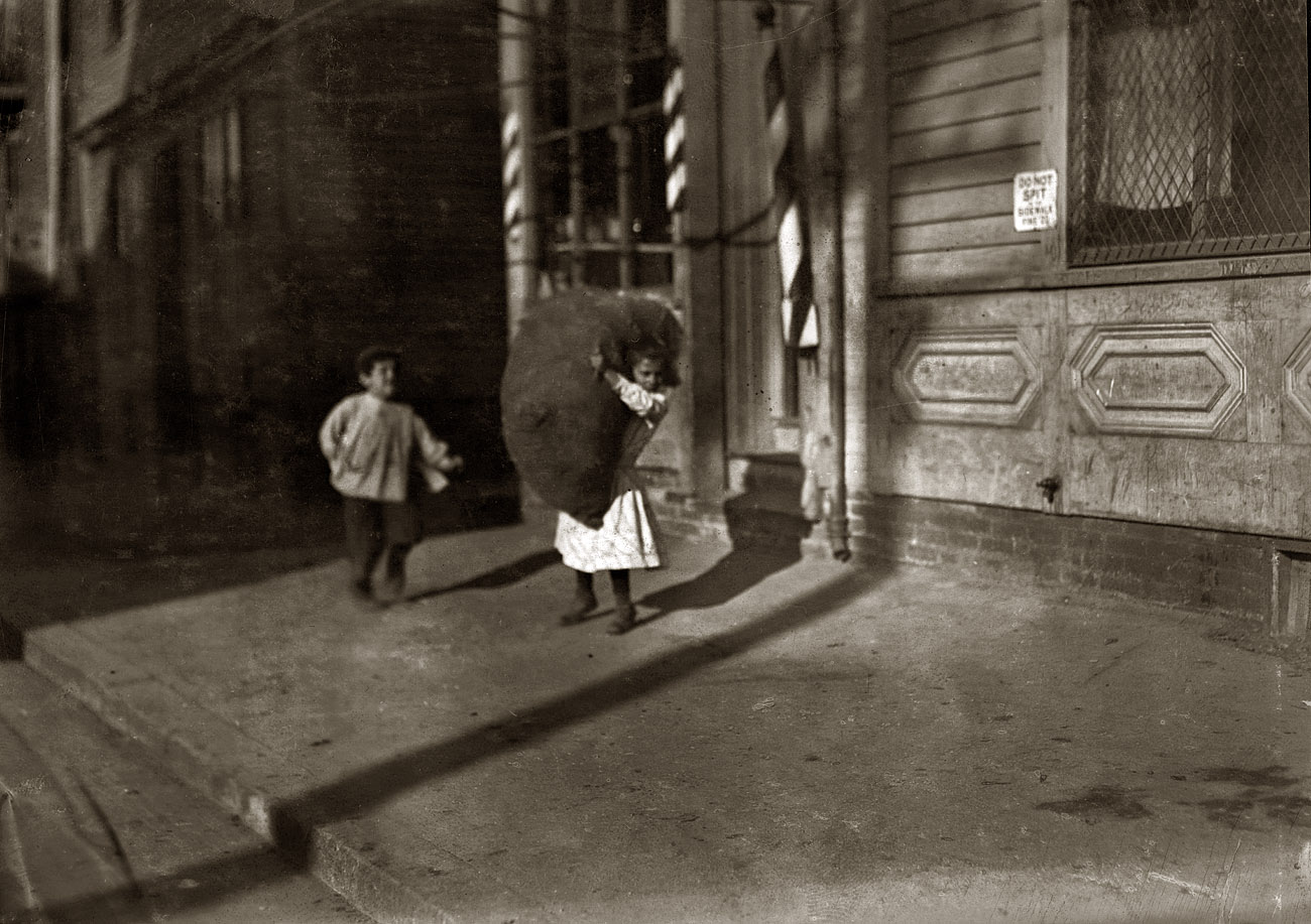 November 1912. Providence, Rhode Island. "Spruce Street. Tiny girl with big bag she is carrying home." Photograph by Lewis Wickes Hine. View full size.