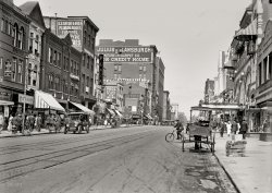 Washington, D.C., 1915. "Street scene, Ninth Street N.W." Among the merchants represented here is department-store magnate Julius Lansburgh. View full size.
Devil in the detailsAnother great Shorpy photo, teeming with robust urbanites, no doubt in early spring. Look at those women. New York's Fifth Avenue had nothing on them! This photo depicts the plethora of transportation modes available in cities in those days. We need to take a cue for our own times, though bringing back the horse could be problematic.
Fixed gear bikesNotice that none of the bikes left leaning against the curb have locks. Imagine trying that today.
AdvertisingI love the painted-on-brick ads. You only see faded ones nowadays - I wonder why they went out of fashion? Maybe they needed touching up too often.
I'm intrigued by the "Backward Season" sign at the importers' on the far left. Was Backward Season a widely-used term for something, or just their own little promotion name à la "Dollar Days?"
["Backward season" was, to judge from the clothing ads in the Washington Post archives, a term used in retailing to describe unseasonable weather in both spring and fall. It was certainly the occasion for a lot of sales. Its last use came in 1955. - Dave]
The CarIt would be interesting to know the make and year of the car on the left of the photo...it appears to be a right-hand drive. I've done some superficial Google images research and can't identify it. Early American cars were produced in RHD. Ford switched to left hand drive production in 1906 and Cadillac in 1916.  What a great image....thanks Shorpy!!
Horse anchorWhat is that cone-like thing on the ground with a rope or something leading up to the horse.  Is that some sort of anchor to make the horse stay put while the driver's inside? Kind of like the anchor of a boat? If not, the question still stands. What is that thing?
I actually think...This is Ninth Street NW looking north.  Just beyond the Lansburgh that's the old Riggs Bank building at the southwest corner of Ninth &amp; F.
[You are correct! I have changed the caption accordingly. - Dave]
Wow, what detail!Horse drawn (no overhead wires) trolley tracks. [The trolleys were electric. See above. - Dave]
Packages at far right perhaps reels of film?  (in front of Washington Film Exchange).  1915 was the year of "Birth of a Nation" so who knows?
Sign for Smyrna rugs is seen 7 years in advance of the burning and slaughter of many citizens of Smyrna, now known as Izmir.  
One of the best.
Horse TetherThat "anchor thing" on a leather strap was a steel weight to temporarily tether the horse, used on milk and bread wagons as well.
Hitching weightThe triangular thing on the ground under the horse is probably a hitching weight, somewhat like this. Just heavy enough that the horse thinks it's tied up, but light enough to transport.
Not horse drawn street carsThe street cars in downtown D.C. ran from an underground feed (see the slit midway between the rails).  As you moved away from the downtown area they raised the trolley pole and switched to the overhead wires.  
Washington Trolleyswere electric by 1915. What looks like a third rail on the tracks is a slot, in which the power line was buried.  The trolley cars had a pickup on a "plow" that projected down into the slot and made contact.  That system stayed in use until trolley service was discontinued in the early 1960s.
Actually trolley power came from underneathTexcritic, the tracks aren't for horsecars. The Washington system was a cable car system with a continuously moving cable underground which each car would engage in order to move. See the "center rail" between the tracks? The gap in that center rail allowed the cars to grab the cable and move.
[Not quite. The streetcars here were electric. Although there was a traction line in Georgetown. - Dave]
Ninth St NWDave, I think this is 400 block of Ninth Street NW looking north.  A few of the businesses I have verified are:

Dean Hats, 422 9th St - Benjamin D. Dean, proprietor
Howard A French, 424 9th St - Indian Motorcycles
Christiani Drug Store, 426 9th St 
Friedlander Bros, 428 9th St  - Men's Suits
S.S. Shedd &amp; Bros, 432 9th St 
Plaza Theater, 434 9th St 
Offterdinger Cigars, 504 9th st - Henry T. Offterdinger,  proprietor

On the right side of the street are Crandall's and Moore's Garden Theaters - seen in this Shorpy photo.
Kodak momentI note on the left of the image a sign offering Kodak film and developing.  Makes me think that someone from that business stepped out across the street to make an impromptu photo.  What is amazing is that for the slow speed of the films (low sensitivity to light) in those days that they were able to get the motion of the pedestrians almost unblurred.  It must have been a very sunny day to get away with a faster shutter speed to freeze the action.
[This photograph was made on glass, not film. - Dave]
Hair splittingI think this is 9th street looking south, taken from the immediate left of the old Riggs building. It's going downhill sharply, and I remember the Gaiety theater being a few doors down from Riggs on the right when looking south.
Those buildings on the left house the Spy Museum.
[This is looking north, not south -- even-numbered addresses are on the left. The Spy Museum is on F Street. The buildings on the left have all been replaced by the J. Edgar Hoover Building. - Dave]

Not Ninth StreetThe photo is of Seventh Street, NW.  Look at the top center for the Lansburgh Dept Store signage.
[This is indeed Ninth Street. You're confusing the Lansburgh department store with the Lansburgh furniture store. - Dave]
+95Below is the same view from December of 2010.
Early FordThe forged front axle is the identifying feature. It is a Ford prior to the Model T. I'm leaning toward a 1911 Touring Car. The very basic design is reflected in Henry's Model B of 1905. That would be about the sixth Ford model produced.
(The Gallery, Cars, Trucks, Buses, D.C., Harris + Ewing, Stores & Markets)