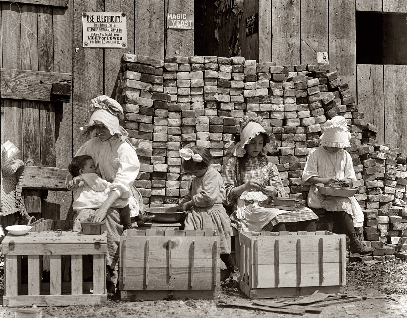 "A mother hulling berries while she nurses her infant. Her other children sit beside her, also at work. Little Mabel Cuthrie [Guthrie?], 4 yrs. old started working last year." Photo by Lewis Wickes Hine, Seaford, Delaware, 1910. View full size.