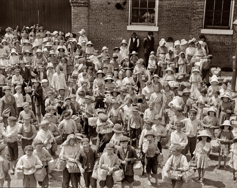 "Dinner-Toters" waiting for the gate to open. This is carried on more in Columbus than in any other city I know, and by smaller children. Many of them are paid by the week for doing it, and carry, sometimes, ten or more a day. They go around in the mill, often help tend to machines, which often run at noon, and so learn the work. A teacher told me the mothers expect the children to learn this way, long before they are of proper age. Photo by Lewis Wickes Hine, Columbus, Georgia, 1913. View full size.
