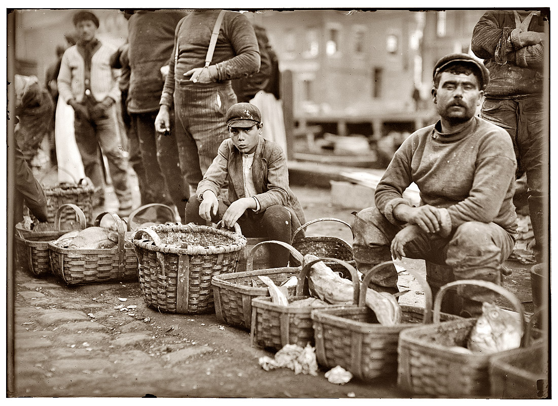 October 1909. Boy selling fish from a basket in Boston street market. View full size. Photograph by Lewis Wickes Hine.