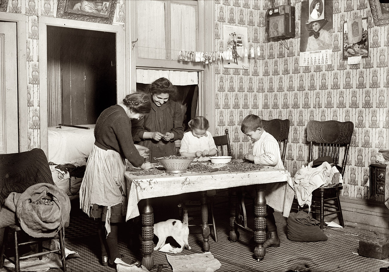 New York, December 1911. "143 Hudson Street, ground floor. Mrs. Salvia; Joe, 10 years old; Josephine, 14 years old; Camille, 7 years old. Picking nuts in a dirty tenement home. The bag of cracked nuts (on chair) had been standing open all day waiting for the children to get home from school. The mangy cat (under table) roamed about over everything. Baby is sleeping in the dark inner bedroom (three yrs. old)." Photo and caption by Lewis Wickes Hine. View full size.