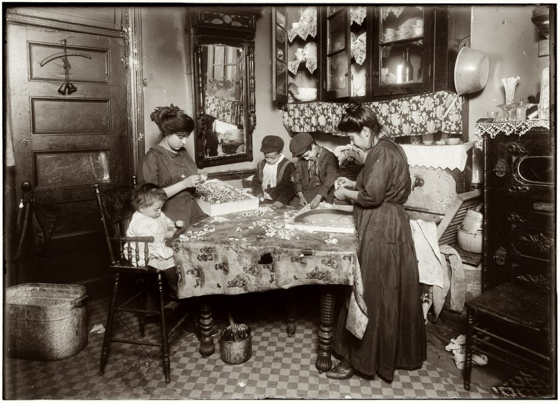 Photo of: 302 Mott Street: 1911 -- December 1911. Family of Mrs. Mette making flowers in a very dirty tenement, 302 Mott Street, top floor. Josephine, 13, helps outside school hours until 9 P.M. sometimes. She is soon to be 14 and expects to go to work in an embroidery factory. Says she worked in that factory all last summer. Nicholas, 6 years old and Johnnie, 8 yrs. The old work some. All together earn only 40 to 50 cents a day. Baby (20 months old) plays with the flowers, and they expect he can help a little before long. The father drives a coach (or hack) irregularly. View full size. Photo and caption by Lewis Wickes Hine.