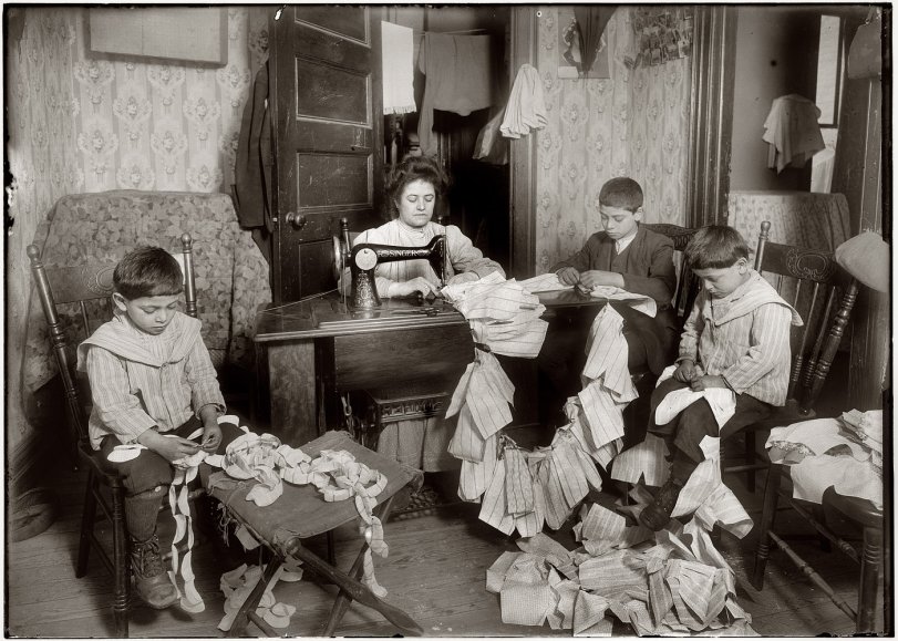 March 1912. "Making dresses for Campbell Kid Dolls in a dirty tenement room, 59 Thompson Street, New York, 4th floor front. Romana family. The older boy, about 12 years old, operates the machine when the mother is not using it, and when she operates, he helps the little ones, 5 and 7 years old, break the thread." View full size. Photo and caption by Lewis Wickes Hine.
