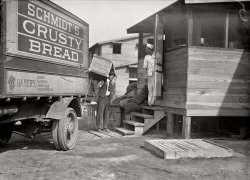 "Camp Meade, Maryland, 1917." Harris &amp; Ewing glass negative. View full size.
Mmm Crusty breadI'm guessing that "Crusty" is a good thing, back then anyway. BTW, put some air in those tires, will ya!
Look at those tires!Dear Lord, look at the tire on the truck.  It appears to be solid rubber.
This means a bone-shaking jolt for the driver every time he runs over so much as a nickel.
Worse:  the wheels will frequently be out of contact with the pavement, making skids far more likely than with pneumatic tires. 
Having to lug 100-pound crates around may be the least of our nattily-dressed driver's issues.
Truck&#039;s wheelsI'm fascinated by the fact that the truck appears to have no tires. I haven't seen many (if any) trucks from this period. It must have been a nightmare to drive.
[The truck has solid rubber tires. - Dave]
Camp to FortI spent the last 6 months of my Army service during the Vietnam War at what was had been upgraded to "Fort" Meade, and was discharged in July 1967. At the time I was living with my wife in Arlington, Va., and commuted daily 40 miles each direction in my Renault Dauphine to make early formation.
Speed , not comfort I can't imagine the spine shattering ride on those tires.
Civilian breadCivilian Bread being delivered to the cook?  When I was in during the Korean mess, all of our bread was made at the Fort Jackson Army bakery and always seemed to be day old.  Got pretty used to it until one happy day the camp bakery  broke down and they supplied us with "civilian" bread.  Man, that was real eating and I have never forgotten that day.  Yummmm!
Also, look at all those sacks of taters that some poor KPs are going to have to peel though I was never assigned to that detail. Fort Jackson (SC) used coal fired ranges while I was there that had to be cleaned once a week by rubbing them internally with brickbats so they would pass Saturday inspection.
Schmidt&#039;sThe Schmidt Bakery is still around, though they no longer hawk "crusty bread". Started in 1886 by German immigrants, it is still family owned (run by their great-grandson) and has bakeries in Baltimore and Fullerton.
Schmidt's potato bread is, by the way, outstanding. Yum. 
Bread for the troopsBread for soldiers from civilian sources is, or was not unusual. My father was an employee of Colonial Bakery in Fort Smith, Arkansas during WWII. The bakery provided bread for nearby Camp (later Fort, now closed) Chaffee. The draft board (or other authority) declared his job as essential to the war effort. As a result, he could not quit his job, the bakery could not fire him, he could not be drafted, nor could he volunteer for the Armed Forces. He was to bake bread for the duration of the war. Since gas was rationed tightly, he sold our car and rode a bicycle to work until the end of the war. He stayed with the bakery for a 49-year career.
Lift That BaleHere we have another guy in a necktie doing some heavy lifting. That crate looks like it's made of wood. His life could have been easier with some sort of cardboard or masonite container.
(The Gallery, Cars, Trucks, Buses, Harris + Ewing, WWI)