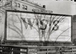 Washington , D.C., circa 1917. "W.S.S. poster." (Aha. So that's what it is!) Harris &amp; Ewing Collection glass negative, Library of Congress. View full size.
Where this isI was able to make out some of the text on that mysterious cornerstone:
UNION OF WASHINGTON O.G.A.S  ….
OF THE MEMORIAL BRIDGE WHICH IN CONNECTING
THE NATION’S CAPITAL WITH ARLINGTON SHA…
and the bottom line ends with
GREAT ARMY OF THE REPUBLIC
Construction of the Arlington Memorial Bridge didn't begin until nearly 10 years after this photo was taken, although plans for the bridge were made around 1901 or 1902.  I would love to figure out the name of the theatre behind this billboard...that might provide a clue about the location.
[From a 1902 article in the Washington Post: "It is the desire of the Stone Cutters' Association that the stone be placed on government property in some prominent location, preferably on Lafayette Square." A cavity in the stone contained Washington newspapers, a Grand Army badge and a copy of the Stone Cutters Journal.   - Dave]

Billboard BubblesThe billboards I see today appear to have much smoother surface than the one in the picture. It seems to have a lot of air bubbles. They must have a much better squeegee system now.
Puzzle SolvedThat's the Belasco Theatre on Madison Place.
http://cinematreasures.org/theater/7618/
Comedy is too easyShakespeare dropped his middle name when he started doing tragedies.
War Savings StampsBillboard for War Savings Stamps to help the war effort.  I still have my War Bond given to me by my parents from World War 2.

Before BondsThat was a shorthand expression for "Buy War Savings Stamps."  Either that, or Microsoft Windows Sharepoint Services is older than I thought.   
CornerstoneThat cornerstone is pretty interesting.  It appears that it is dated as 1902 (MDCCCCII), yet the picture is dated 1917.  I also notice that the cornerstone edges are protected by wood cornerguards as if it getting ready to be installed, yet the billboard latticework was cut out to accommodate the stone, implying it was there before the WSS! advertisement. 
War Savings Stampswere sold in both WW1 and WW2 to help finance the cost of the wars.  They came in 10 and 25 cent denominations, and were aimed at school children.  During WW1, the Boy Scouts were heavily involved in promoting and selling them.
During WW2, you could paste them into special booklets and, when filled, the booklet could be redeemed for a $25 War Bond.  I was very proud when I got that Bond, doing my kid bit to win the war.
(The Gallery, D.C., Harris + Ewing)