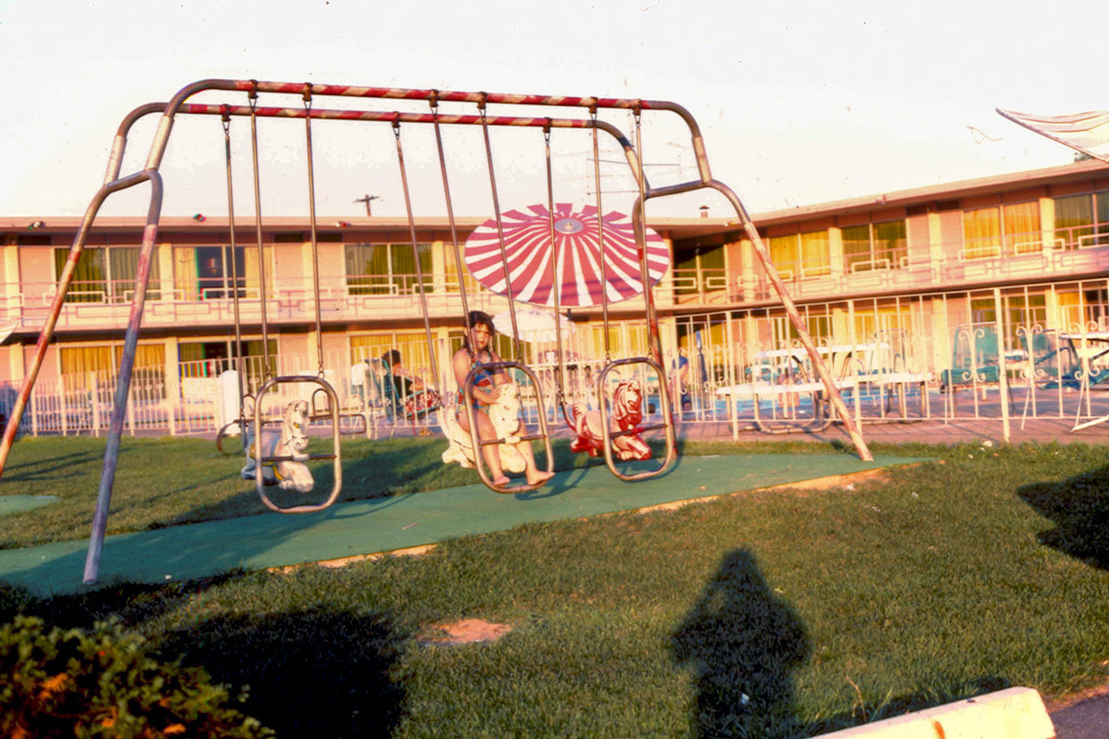 This is me on a swing at a motel in either Maryland or Delaware sometime in the mid-1970s. It was likely taken by my father, whose shadow appears in the photo, too. I really like this photo -- the sun, the motel architecture (is that an oxymoron?), the photographer's shadow, and especially the red and white pool umbrella. Doesn't it all just scream 1970s? View full size.