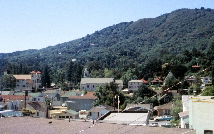 I was 11 when my brother took this Anscochrome slide of Larkspur, California, where I grew up. Around then I might have gone to the twin-towered City Hall at left, either to the Library to satisfy my curiosity about freeways, dinosaurs, coins or, believe it or not, peruse collections of New Yorker cartoons, or to the city offices to bug the clerks for copies of city forms I could adapt for the make-believe city I incorporated our yard into. Alongside is the fire house, where I might take pictures of the trucks. Across the street is St. Patrick's church, where I'd fidget during Mass every Sunday. Our house was a block away, hidden by the trees. Farther along, the steep-gabled building is the old St. Patrick's, where once a week fellow Catholic kids and I on religious instruction release from our public grade school would attend Catechism classes where stern nuns would attempt to drill dogma into our little souls. Below the church, the Ford woody is in the parking lot behind the Rainbow Market (red roof at left), where earlier my father worked for a few years. Down center, the small roof with the flag pole is the then-new Larkspur Post Office building. And then, a 1956 Pontiac. View full size.
