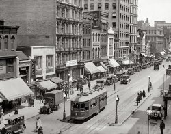 Today we're leaving the office and taking the streetcar downtown for some shopping.  From 1924, "F Street N.W. from 14th Street." View full size.
Swastika Truck IIPossibly made by Detroit's K.R.I.T. Motor Co.

[Looks more like an electric truck. Maybe a Walker Electric. There's no radiator. - Dave]

Arthur Burt Co.I found these three early 1920 ads for the Arthur Burt Co., in the Washington Post. 
Lisle ribbed hose, of fine texture, for women and juniors: black, white, brown, elk, gray and navy blue. Just right. 
Shoes and hose of today, Arthur Burt Co., 1343 F. Dependable military footwear, "Nature-Shape" school shoes.
The "Tuiriwun," a slipper in black satin or patent leather that is correct for both evening and street wear and, consequently, much in demand. $9.00. Arthur Burt Co.
The BartholdiHey, it's the Bartholdi Cafe, offering seafood and shore dinners, inviting ladies and gentlemen, and open Sundays.  I learned this stuff from a billboard next to the Texaco station.
I wondered what the "ladies and gentlemen" on the sign meant - no rowdies and ruffians, no wenches of questionable virtue? A 2005 Washingtonian article mentioned the Bartholdi (it was characterized as "early 20th century" seafood, apparently not the best).
Truck SwastikaThat truck pulling out near the guy crossing the trolley tracks has a swastika on it. Was there an automotive company that used that emblem before it was abused by the Nazis?
[Use of the swastika as a decorative motif or commercial insignia goes back long before the National Socialist Party adopted it as an emblem. - Dave]
Health Week starts April 28 1343 F St.: Arthur Burt Co.
Footwear for "society affairs," afternoon or evening.
1341 F St.: Bartholdi Cafe
Washington Post, May 30, 1923: Advertisement

This if the first holiday since we've extended our service to include the ladies.  Bring them in and let them enjoy the Bartholdi famous shore dinner or a selection of the Sea Food delicacies served our way.

1339 F St.: H.W. Topham
Trunks, suitcases, traveling bags, hot boxes, etc.
1337 F St.: Watters Sterling Boot Shops
"The kind of shoes you want at the price you want to pay"
1333 F St.: Adams Building
Washington Post, Apr 27, 1924

Health Week Campaign Gets Start Tomorrow
"Health Week" starts tomorrow.  Agencies participating took possession of the old Y.W.C.A. home, at 1333 F street northwest, to install free exhibits and motion pictures, which will run through the entire week.  A large sign advising "Keep the Well Person Well" and "Get the Sick Person Well" placards the building, which is open from 10 a.m. to 11:30 p.m.

1331 F St.: Meyer's Shop
"Everything for well dressed Man and Boy" - Rogers Peet Clothing
1329 F St.: Franklin &amp; Co. Opticians
1319-1321 F St.: Interstate Building
The Young Men's Shop on ground floor
Washington Post, Jan 9, 1912

Plans for the construction of a ten-story office building on F street ...  When completed the new building will have cost approximately $600,000.  The Interstate Commerce Commission, it is expected, will lease quarters in the new structure.

1315-1317 F St.: Baltimore Sun Building
Contemporary Photo
Washington Post, Apr 9, 1903

The Baltimore Sun building, 1315 and 1317 F street was sold yesterday afternoon at public auction to Walter Abell.....The Sun building is perhaps one of the best known office buildings in Washington and one of the most substantial in the country. ...  It was built in 1887, the jubilee year of the Baltimore Sun by the founder of the paper, Mr. A. S. Abell,  ...

Washington Post, Jul 12, 1987

The oldest standing skyscraper in America - maybe the first --an exquisite nine-story example of eclectic Victorian architecture, is celebrating its 100th anniversary this year. Although New York and Chicago are normally associated with skyscrapers, the oldest example is in neither city but rather in Washington -- the Sun Building at 1317 F  St. NW.
...
Now restored to its original elegance, the Sun Building gives a hint of what Washington was like before the homogenizing influence of post-World War II architecture began erasing the city's history. Built by A.S. Abell, publisher of The Baltimore Sun, it originally served as a home for the newspaper's Washington bureau. Upon its completion in 1887, The Baltimore Sun Hershel Shanks, a lawyer and part owner of the Sun Building, is editor and publisher of the Biblical Archaeology Review. declared the building "the most imposing private structure in the national capital."

Safety LastDig the scaffolding set up with no safety barrier or safety roof, only a few paper signs stuck to it that probably say "Watch out for stuff falling on your head," or possibly something more appropriate for the period, like "Mind the head."
Hey, there was a cop standing on the corner in the Patent Office photo too. At least this street is safe from horse thieves.
It looks like a breezy day.It looks like a breezy day.  See how the coats and awnings are billowed?
WowGreat shot.  The crispness and detail in these old photos is still startling. 
Frederic Auguste BartholdiHotel Bartholdi appeared in the Metropolitan Life 1908 Shorpy photo. In this one he's a Cafe for Ladies &amp; Gentlemen. He was the sculptor of the Statue of Liberty. It's 1924 and there are no horses in this picture. Were they banned from these streets?
Checker CabsBoth of the two-tone taxis are Checkers, made by the Checker Cab Manufacturing Co. of Kalamazoo, as is the taxi in the extreme lower left hand corner.  By 1924 Checker was building 4,000 40 hp cars a year at an average selling price of about $2350.
The bus&#039;s power polesThe bus's power poles are down.  It must convert to gas power when overhead power lines aren't available.
[That's a streetcar, not a bus. Downtown, where there were no overhead power lines, the electrical supply was under the street. More info in the comments here and here. - Dave]
TrolleyI notice there are no overhead wires for the streetcar.  Apparently it was powered from a third rail on the ground.  Seems pretty risky on a public street.
[The power supply is underground. Not a rail, and not risky. - Dave]
Third rail again?Oh Dave, you have the patience of a saint.  How many times must one answer the same questions regarding streetcar power.  I think its overly due time for some default link to background information regarding streetcar engineering in the District of Columbia.
A few of the previous explanatory postings on Shorpy: [1,2,3]
StreetcarFor those interested, the streetcar pictured in this scene is Washington Railway and Electric Company car number 602. Built in 1912 by J.G. Brill Company of Philadelphia it was delivered on September 21 of that year. In 1912 this streetcar cost $6016.17.
In 1933 the Capital Traction Company took over streetcar operations in Washington DC and WRECo 602 became Capital Traction Co. car 836. In 1935, 836 was assigned to the Brightwood Division. By 1939, it was assigned to the Navy Yard Division, and in 1942 to the Benning Division.
The centre door meant that 836 required two-man operation - a driver, and a conductor - and by the 1940s these older, slower cars were also creating bottlenecks as the newer, faster cars lined up behind them. 836 along with the remaining centre door cars were retired in 1944 and scrapped the following year. With the retirement of these cars retired the last of Washington DC streetcar conductors, as now all the cars were one-man operation. Not only were the cars faster, they were now cheaper to operate.
One centre door streetcar, CTC 884 former WRECo. 650, is currently held by the National Capital Trolley Museum in Wheaton MD. It is currently unrestored as far as I know. See it soon for the museum is closing December 1 due to construction of the Intercounty Connector, and it is not scheduled to reopen until next summer.
Sources cited:
Peter C. Kohler, "Capital Transit, Washington's Street Cars The Final Era: 1933-1962" Bonifant MD: National Capital Trolley Museum, 2001.
National Capital Trolley Museum: http://www.dctrolley.org/
Streetcars &amp; Hobble SkirtsThanks James for all the information about car #602.  In the photo, it appears that the lower step folds up while the car is in motion.
 Washington Post, Mar 20, 1923

Order Low-Step Cars
 W.R.&amp;E. Officials Accede to Demand of Women
Fifty are Now Being Built


The women of Washington have won a victory in their demand for street cars with lower steps.  The Washington Railway and Electric Company has placed an order for 50 new cars with the J.C. Brill Company, of Philadelphia, specifying particularly that the cars be constructed with low steps.
The operation of the new style cars throughout the city undoubtedly will meet with the hearty approval of the women, who have been making a strenuous fight for more than two years to abolish the high steps.
The new cars are being built as rapidly as possible, and the first shipment is expected to arrive here about April 15.  The cars are what are known as the Narragansett type, being semi-convertible from closed to open, of double truck, and capable of comfortably seating 80 passengers.  The seats will run crosswise, and the exterior will be painted yellow.
It is announced by an official of the company that the cars will be constructed with two steps, affording easy ingress and exit from the vehicle.  Upon just what lines the new cars will be operated the officials have not decided yet.  A number of the cars, it is understood, will be placed on the Georgetown and Mt. Pleasant lines to replace those recently destroyed in the fire at the car barn at Thirteenth and D streets northeast, in which 80 cars were burned.
"We have ordered that the new cars be constructed with unusually low steps," said an official of the Washington Railway and Electric Company, yesterday, "as we realize that the plea of women patrons, who ask for lower car steps, is justifiable.  The new cars will be constructed, in so far as the steps are concerned, to meet the approval of the women.  Later in the year we will either order additional cars of the low step type, or remodel the cars now in service to comply with the request of our women patrons."

 Washington Post, Apr 26, 1923

New Car Tested Here
Hobble Skirts No Barrier to Improved W.R.&amp;E. Vehicle


"Wearers of the hobble skirts," said W.F. Ham, vice president of the Washington Railway and Electric Company, "will have no difficulty in boarding our new car, which we have just tried out for the first time.  It has so many features that are new that we are delighted with it.  During its trial trip yesterday afternoon, it carried no one but the officials of the company, but within a few days, we will run it in with our regular service, and then ask the passengers for their opinions.  If they are favorable, undoubtedly we shall add a great many more of such cars to our rolling stock."

Bartholdi HotelMy family owned the Bartholdi Hotel. My great-grandmother was Theresa Bartholdi. There is an old family tale that Vincent Sardi of Sardi's Steak House was a cook for the Bartholdi and met his wife who was a maid there.
(The Gallery, Cars, Trucks, Buses, D.C., Natl Photo, Streetcars)
