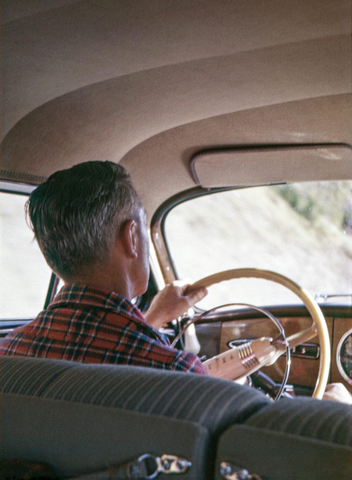 My father piloting our 1949 1948 Hudson. Looks like he's in the midst of shifting. Dig that cool steering wheel and faux-woodgrain dash. Removing the slide from the mount for scanning revealed the appendages on the backs of the front seats, which I'd forgotten about. In fact, I'm still hazy about what they were; the one on the left looks like it's holding something. My brother's Ektachrome slide. View full size.