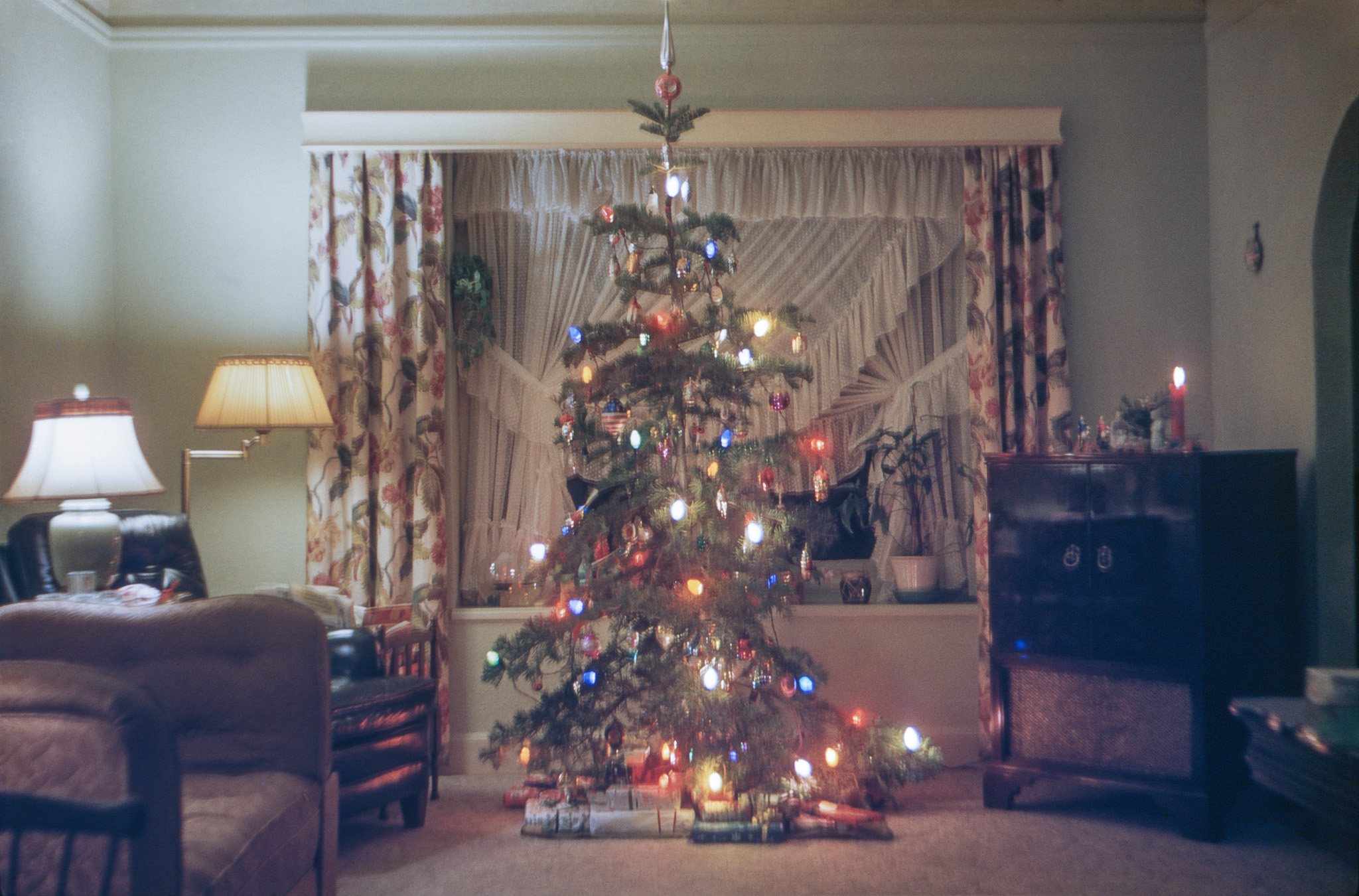 December 1955. Here's our family's entry in the Shorpy Christmas tree sweepstakes. Devoid of any jolly celebrants, unfortunately, but at least we have my mother's curtains and drapes. Many vintage ornaments are in evidence: Santa heads, houses, a table lamp, a mushroom, an angel, a prizefighter, some birds with spun glass or celluloid tailfeathers, and one of my personal favorites, a big one we always called "the stars and stripes forever" on the left a little more than halfway up. Some were from my Mother's family and dated back to the early 1900s, including one that still had wax drippings on it from when you actually lit your tree with candles. On the right, our Motorola hosts the Nativity scene complete with plastic Wise Men. Sharp-eyed observers may note that on the window seat, the fishbowl, vacant a year later, here appears to be inhabited. My brother recorded the available-light exposure details for this Kodachrome slide on the mount: f2.8 @ 1 second, during which he jiggled the camera slightly. View full size.