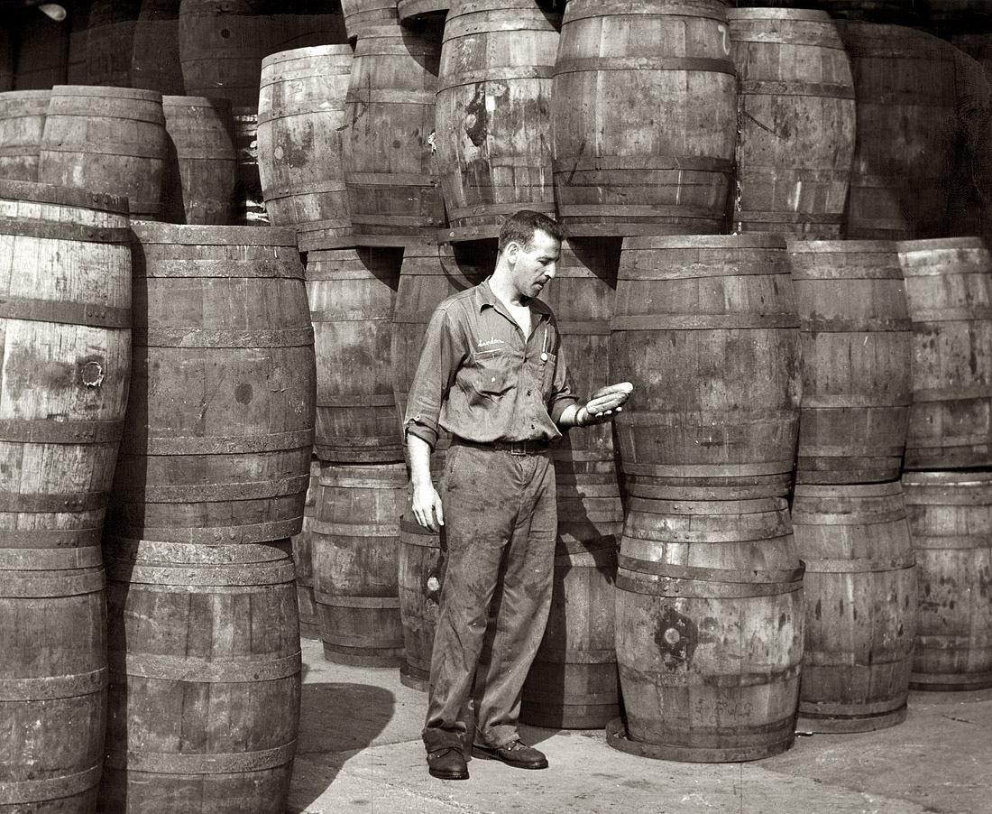 New York, 1959. "Stanley Hyams, co-owner of Washington Pickle Works, holding two pickles in a roomful of barreled dills." Photograph by Roger Higgins for the New York World Telegram & Sun. View full size.
