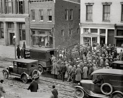 January 31, 1925. Washington, D.C. "Police raid on gamblers' den. E Street between 12 and 13th." National Photo Company glass negative. View full size.
Where are the newshounds?Nobody tipped off the press?  You'd think there'd be a few Speed Graphics popping away at that Jazz Age perp walk.
[Who do you think took this photo? - Dave]
Call my lawyerLooks like the Kingfish, Andy and other members of the Knights of the Mystic Sea are in big trouble.
How convenientYou could launder your winnings next door.
ShowtimeThe onlookers seem to be enjoying this immensely.  Probably thinking "There but for the grace of God or throw of the dice go I."
Delco-Light?Strange to see a "Sales Branch" in a major city, since the Delco 32-volt battery-charging generator catered to a rural market. The New Deal's REA finally put an end to that business in the late '40s.
[The store sold refrigerators, not generators. Frigidaire was a subsidiary of Delco-Light. - Dave]
There&#039;ll be standing room onlyin that paddy wagon.
You Missed Me!Looks like the guy in the second floor window is taking one more look before his getaway.
Thoroughly integratedShoulder to shoulder, blacks and whites enjoying the spectacle together. Couldn't even do that in a movie house. 
Saturday nite fish fryWhen I look at this picture, I can't help but hear Louis Jordan and his orchestra singing about the fish fry getting raided!
Old D. C.I've always heard that Washington was thoroughly Southern and segregated, but the folks in this scene seem to be mixing without much regard to race, and everyone appears to be equally well-off, as far as clothes are concerned.
Frozen assetsGeneral Motors entered the refrigerator business at the start of WWI, anticipating that the government might ban the private ownership of automobiles as an austerity measure during the war. There is an interesting discussion of this in Alfred P. Sloan's classic "My Years with General Motors."
Quick Lunch PlusWith your lunch, just deserts are served.
The other showDespite the big show on the sidewalk, several people in the crowd are obviously focused on the photographer.  Makes you wonder if he was hanging out of a window too.
More Fugitives?It looks like there may be even more culprits that escaped the dragnet. Look behind the door of the Delco building, the second story window of the Delco building and possibly peeking around the column of the Cohen Hughes building.
Luck be a lady!Nicely-Nicely and good old reliable Nathan, 20 years earlier:
"If the size of your bundle you want to increase,
he'll arrange that you'll go broke in quiet and peace."
And, most appropriate since it's in a lunchroom:
"There's and awful lot of lettuce for the fellow who can get us there."
Jail His A*sThere's one guy in the picture without a hat, arrest him, he's the culprit.
LurkersIt's really hilarious, the four guys hiding out to the left. There a shady character in the door, someone in the window above, the somewhat obvious guy standing on the ledge and then the guy hiding behind the column.
(The Gallery, Cars, Trucks, Buses, D.C., Natl Photo)