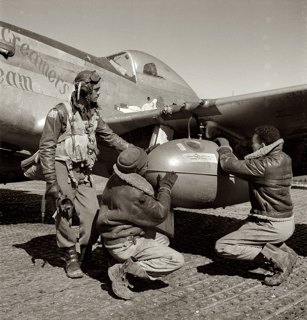 March 1945. Ramitelli, Italy. 332nd Army Air Forces Fighter Group. "Tuskegee airman Edward C. Gleed of Lawrence, Kansas, Class 42-K, with two crewmen adjusting an external 75 gallon drop tank on the wing of the P-51D Creamer's Dream." View full size. Medium format negative by Toni Frissell.