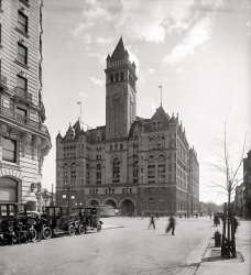 The Post Office building in Washington circa 1911, about the closest the District of Columbia ever came to having a skyscraper. Harris &amp; Ewing. View full size.
AD 1897Notice the "AD 1897" over the door; it was about 14 years old at the time.
Taxi, anyone?The three cars in the foreground may be taxis. Is that a fare box in front of the window on the middle one? I also notice that the people just walk wherever they want in the streets. They have sidewalks but do not feel motivated to use them.
The grandest of them all!Seems like government or public architecture in the period this building was built used the same box of parts.  Town Halls, schools and post offices all looked very similar. But I have never seen anything approach this in scale.  It surely must be the grandest of them all!  The life span of these buildings was relatively short. Was it because conversion to newer heating/cooling systems was impractical?  
Car vs driverThese cars have the look of horseless carriages. 
I'm surprised that the manufacturer saw fit to provide a roof over the head of the driver, since they didn't make any other concessions to the comfort of the person operating the thing. 
[That's the town car body style -- open driver's compartment, enclosed passenger compartment. - Dave]

UnthinkableThere was a move at one time to tear this wonderful building down!  Cooler heads prevailed!!
Railway Post OfficeThe white blur in front of the building is a Pennsylvania Avenue railway post office, or R.P.O.  The streetcars in Washington as well as several other cities that carried mail and no passengers were painted white. Mail was sorted by a clerk in the car. Letter mail received en route was postmarked aboard the trolley and dispatched to post office stations located near the route.
The "old post office" building served two roles.  The offices at street level and above were the Post Office Department headquarters.  The building also served as the main post office for the District, with retail windows through the doors up the steps at the front, and a workroom floor in the core of the building and below street level.  Loading docks were at the rear for city deliveries as well as wagons to the railway stations.
The mail processing activities and main post office functions shifted to a new building at 2 Massachusetts Avenue N.E. after Union Station was opened.  The Post Office headquarters relocated to a new building across the street to the right in this view, completed in 1932.
Frank R. Scheer
Railway Mail Service Library
Cheer, cheer for old Notre DameIt was designed by Willoughby J. Edbrooke, the same architect who designed the Golden Dome at Notre Dame. 
Go visit it!The building is still there--and not only that, the Post Office Pavilion building is open for visitors. The ground floor has a few retail shops and restaurant vendors.  Or you can take 2 separate elevators up to the bell tower and look at the beautiful view of Washington. All free too. http://www.oldpostofficedc.com/
(The Gallery, D.C., Harris + Ewing)