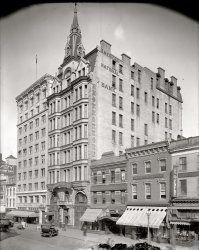 Washington circa 1918. "American National Bank, F Street." Right next door to Harris &amp; Ewing Photographers, who took so many of the photos (including this one) seen here on Shorpy. Harris &amp; Ewing glass negative. View full size.
Still There?Please tell me this wonderful building is still there!
["This wonderful building is still there!" - Dave]
View Larger Map
Victor E. Desio &amp; Co.


Desio &amp; Co. will Remodel Dwelling

Victor E. Desio &amp; Co. have plans prepared by Julius Wenig, architect, for remodeling the three-story and cellar store building at 1309 F street northwest.  The entire building, which is 26 feet wide by 82 feet deep, will be remodeled into two stores.  The front will be of all glass show windows, marble base and copper trimming.  The second and third floors will be fitted out for store and work rooms, and an electric elevator will be installed from the first to third floor.  Metal ceilings and marble floors will be a feature on the first floor.  
When completed the work will represent an outlay of $8,000.  Work will be started July 12, and Victor E. Desio &amp; Co. will occupy the west store and Howard Deane the east store by September 1.

Washington Post, Jul 9, 1916 



Victor E. Desio Rites Arranged Here Tomorrow

Victor E. Desio, retired jeweler, who for many years conducted business at 1309 F street Northwest, died yesterday at his home, 2400 Fort Scott Drive, Arlington, Va.  He was 64 years old.
Born here, Mr. Desio carried on the jewelry business founded by his father, the late Gerome Desio, in 1874. He was a member of the Holy Name Society and the Lido Civic Club.

Washington Post, Jan 19, 1943 


Not Entirely ThereThat wonderful steeple -- was this a cathedral of banking? -- is gone.
Motorized bicycleCheck out the motorized bicycle at the far right.  The more recent Schwinn Heavy Duty or the Worksman bikes look like that.
Sidewalk sidecarCheck out the bike with the cargo sidecar in front of the bank! And what are those brass cans on the sidewalk?
[Fire extinguishers. - Dave]

Motor PlacementMotor is mounted on right front fork.
AKA Baltimore Sun Bldg.Originally built for the Baltimore Sun newspaper.  Alternate Shorpy view in 1924.



Bank In Sun Building
American National Acquires F Street Structure

The American National Bank has bought the Baltimore Sun Building, the price it is understood, being between $210,000 and $225,000.  The bank will remodel the interior of the building, and will take the entire two first floors for its bankroom, giving it one of the largest rooms, if not the largest in the city.  The bank will move into its new building in September or October of the present year, the deed for the purchase of the big office building, one of the finest in the city, and one of the landmarks of F street, is consummated practically on the first birthday of the bank, its first year of existence having ended yesterday.  The bank has been looking for a new location for some months, its present building on Fourteenth street not being large enough.
...
The building was the first of the "tall buildings" erected in Washington, and when it was built, about twenty years ago, it was the handsomest business buildings in the city.  It cost for the actual construction about $340,000.

Washington Post, May 5, 1904


BicycleI see the bicycle, but having trouble locating the motor. Maybe he took it with him while he was shopping.

Motor BikeI'll be. It looks like a Smith Motor Wheel. They were usually mounted at the rear of the bike. I've never seen one up front. Just like the one that the lovey Ms. Young has on her Bug.
Dayton Motor BicycleThat's a very rare Dayton Motor Bicycle. The motor is indeed very similar to the Smith Motorwheel, but it was a version sold by the Davis Sewing Machine Company, makers of the Dayton brand at the time. The engine is in the middle of the front wheel. The patent is here.
(The Gallery, D.C., Harris + Ewing, Stores & Markets)