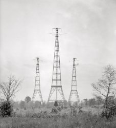 Arlington, Virginia, circa 1917. "Radio." Masts for the Navy's wireless station, built in 1912 at Fort Myer. Harris &amp; Ewing glass negative. View full size.
Questions Could it have been in contact with the Titanic, or was it too early? How about the Lusitania or other ships in distress? Was it used in WWI? What were its accomplishments?
Wireless TelegraphyThe Navy's wireless communiques transmitted over the Fort Myer and Chollas triatic antennas, and well as ship to shore, were all sent with telegraph keys using Morse Code and naval encrypted telegraph codes. For the inaugural commissioning ceremony at Chollas Heights, a special sterling silver and ebony telegraph key was created by a local jeweler. Voice and other forms of data transmissions between these stations would come much later. 
Old FaithfulA concise history of early Navy wireless.
The signal from NSS at Arlington was audible across the country.  I used to hear it easily in Kansas.... the rhythm of dah-dit dit-dit-dit dit-dit-dit remains in my memory like a favorite song.
[I think you linked to the wrong article. - Dave]
Fort Myer&#039;s Twin SisterIn 1917 the triatic antenna at Fort Myer was linked to a series of similar wireless station antennas that allowed the Navy to communicate with Pearl Harbor and the Philippines. San Diego provided the transcontinental relay to Hawaii with the Navy's 600-foot triatic antenna at Chollas Heights (a few miles east of San Diego Bay), seen here in a San Diego Historical Society "Journal" image. On Dec. 7, 1941, the Chollas antenna relayed the news from Pearl Harbor to Fort Myer, and remained in use until the 1970s. It was demolished about 8 years ago to make way for a naval housing project. The three 600-ft. towers supported a solid copper wire, the actual antenna element, suspended vertically between them from the top level down to a radio room on the ground. Those little horizontal catwalks at the top of each tower in both photos were 32 feet wide.

Naval Dreams

Navy Will Erect a 600-Foot
Tower at Fort Myer

A powerful wireless telegraph station of the navy, capable of communicating with naval vessels 2,000 and possibly 3,000 miles distant from Washington, will be erected at Fort Myer.
The high-power plant will be designed to keep the headquarters of the American navy in close touch with war vessels in the Atlantic Ocean.  It has been the dream of naval officials for years to erect such a station in the environs of the National Capital.
At one time it was suggested that a wireless mast for the purpose be constructed on top of the Washington monument, but strenuous objections were raised to the proposition, and several sites have been suggested since and discarded.
 ....

Washington Post, Mar 27, 1911 



Will Build 3 Towers
U.S. Wireless Plant at Arlington to Eclipse Monument

The construction of three wireless towers to be erected on the government reservation at Arlington by the Navy Department will mark a new era in electricity.
The towers will be arranged in the form of an isosceles triangle, the central one being at the apex and standing 600 feet over all.  The other two towers will be each 450 feet in height and self supporting; that is, there will be no guy ropes of any kind reaching from one tower to another.  Some idea of the massiveness of the frame work in the towers may be gathered from the fact that 900 tons of steel will be used in the construction.  Notwithstanding this fact, they will not be bulky, but will present a pleasing appearance of a delicate cobweb tracery against the skyline.  The original plan called for towers of reinforced concrete, but as one of the structures will be higher than the Washington Monument, patriotic naval officials decided that a change of idea would be necessary to avoid detracting from the memorial to the first president.
...

Washington Post, Jun 13, 1911 


War of the Worlds!Three machines, striding across the misty landscape and  the leader, with arms outstretched, about to tromp on an unsuspecting household.
VLF transmittersVery few are left. There's one preserved in Sweden, still used one day every year.
http://en.wikipedia.org/wiki/Grimeton_VLF_transmitter
What a rare treat !  I love this!I am the radio System Manager for Arlington County, Virginia, and I needed to thank you for the photos at Fort Myer, in San Diego, and the newspaper article from 1911!  To be able to peer into 1917 and see those towers is a gift.  We cannot build towers in our urban Arlington any longer, but must use existing office buildings for our radio sites.  Thank you for this, it is meaningful in so many ways.  I only wish my grandfather were here to ask if he remembered them!!  A big thanks to my co-worker, Paul, who found this site.
TimeclockThe Arlington, Va. towers sent out a regular time signal from the clock at the National Observatory.  Weather reports were also broadcast.  Permitting others to synchronize with an official time was significant.  Time of day is a subtle empire thing.  You just cannot imagine the difficulty created when there is no settled arbiter to declare the top of the hour.
["Subtle empire"? - Dave]
San Diego tower sistersI was in San Diego and watched a similar set blown up in the 90s. They were the ones that had recieved and passed on the news from Pearl Harbor.
(The Gallery, Harris + Ewing)