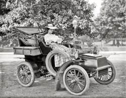 Washington, D.C., circa 1908. "Miss Corine Murphy in auto." Note the unusual rear tire. Harris &amp; Ewing Collection glass negative. View full size.
Portable treadsThose tires solve the problem of having to throw away perfectly functional "Goodyear Quick Detachable Tires" just because the tread is worn out.
All four tires are slicks and the tread (sort of like putting chains on a car today) is added to only the drive wheels. Makes sense. And you can have dirt road tread, and cobblestone tread, and asphalt tread, depending on where you plan to drive.
But I like that huge radiator best with the gaping spaces to its core. Not to mention that this car is from before the era of bumpers.  You hit somebody with that radiator first. If you hit a horse, he'll get a behind branded with radiator textured plaid.
Ms. MurphyLooks more than ready to lay down some serious miles.
Cadillac Model B RunaboutCirca 1904.

Not quite KodachromeIt was too hot and windy outside to work in the yard so I spent the whole day coloring this old photograph. Thats my excuse and I'm sticking to it.
OvertiresI think they are galoshes to keep the mud off your good
"Sunday go to meeting" tires.
189The license plate number is written on the headlights. 
It&#039;s an outrage!Next thing you know they'll be wanting the right to vote, and before you know it liquor will be against the law!
Snakeskin traction sleeves"Viper" was one popular brand. Flayed from live boa constrictors, which were grown on python plantations in Cuba around the turn of the century.
Slick TiresThey appear to be "Billet" detachable tire protectors with "contre envelope" attachments or similar.  ("The Horseless Age" Volume 15,  January 4, 1905)
The "tread" part has flaps which extend over the sidewall on both sides and hold a wire extending around the circumference and fasten (tighten) in two places with a screw and nut.
At that time here were many types of tire protectors of various designs and attachment schemes.  Some also claimed to improve traction.
An old friendThis is the second car we've see of this general type. The other was in front of the Gotham Hotel a day or so ago. I wonder how many of them were made.
Oh, Say, I Can See!I would suggest the centre headlight on the swivel burns acetylene, furnished from a carbide and water gas generator on the auto's left side, the top of which is just visible over the dash.
Water in a reservoir on top is controlled to drip onto carbide chunks in the base, which generates acetylene gas. A pipe and a hose would bring the gas to the lamp within which is a ceramic burner jet for the flame.
Thank You again for another wonderful photo from long ago!
(The Gallery, Cars, Trucks, Buses, D.C., Harris + Ewing)