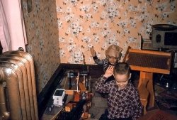 Here is a picture of younger brother George, and I, playing with our "shared" American Flyer c.1958. The "steam" locomotive and tender cannot be seen, but on the floor you may spot several familiar items: signal bridge, telephone pole, water tower, small trackside tool shed. There are two windmills made of tinker toys, too. We had a cow that would block the track and quickly move out of the way when the train approached. Also in the room, with fanciful wallpaper, note the steam radiator, the peg desk and the record player. Burl Ives' "Bimbo" is probably playing. What imagination! What fun! 
Kodachrome slide taken in Clinton, Iowa, c.1958. View full size.
Still usefulMy kids have that peg desk (with a chalkboard lid). A number of desired Lego kits are currently listed on it.
I don't think they've ever seen an actual steam radiator.
(ShorpyBlog, Member Gallery)