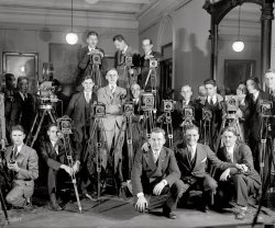 March 28, 1929. "Cameramen, Stimson office." Photographers on the occasion of Henry Stimson's swearing-in as Secretary of State. Nat'l Photo. View full size.
Bill Murray... call your office. Isn't that him crouching down front and center? But, seriously, aren't those mostly Speed Graphic cameras? Ah, the days of 5x7" film stock, no feeble 35mm here. Except, perhaps, that movie camera, the film magazine looks a bit wide for 16mm.
[Most of the guys would have been using glass, not film, in 1929. - Dave]
Is that Carl Spackler?The guy squatting in front looks like Bill Murray during the Caddyshack era.
At the MoviesThose are both 35mm movie cameras. Interesting that one is sound and one a silent (hand-cranked, second from the right). The sound film still exists in the Fox Movietone collection at the University of South Carolina: 
Interior: medium shot man helps get everyone in place. Medium shot Supreme Court Chief Justice William Howard Taft administers oath of office to Henry Stimson, the new Secretary of State. Note: emulsion deterioration throughout. B&amp;W, Sound, 5.11 minutes
Wooden TripodsThese still camera statives (I own one dated about the same era) are very stable, yet much lighter than their modern versions, included the carbon fiber ones. The movie cameras, off course, are 35 mm. Still the hand held Arri started in the '30 as 35 mm movie cameras.
IronicThere's something kind of ironic about a photo of photographers.
Speed GraphicsThose all look like 4x5 inch Speed Graphics. They produced a newspaper-sized contact print, so it was a lot faster to get a photos in the paper using them instead of a 35mm camera, which would have required enlarging the tiny negatives.
Note that a few are mounted sideways on the tripods to achieve portrait framing instead of landscape.
[Another reason not to use a 35mm camera would be that they didn't exist here. - Dave]
Let There Be LightCould not help but notice ... no flashgun, no flashbulbs, no strobe light! Surprised they are using glass and not film, give them credit, they certainly had excellent results which we today should all appreciate.
[They seem to have used some sort of auxiliary lighting -- look at the shadows. I found a second glass neg that came out a tad dark. - Dave]

Where.......is the esteemed and mischievous goat?
Speed GraphicMost of the still cameras can easily be identified as 4x5-inch Speed Graphics, from the size and visible controls for the focal-plane shutter.  Perhaps interestingly, only one is loaded - the center camera in the rearmost/topmost group.
The flashbulb had been invented in Europe the year before, but wouldn't make its way to the Americas until the next year.  This looks to have been lit from two directions - possibly floodlights, probably flash powder.
Ah, the good old days...
I actually prefer the "dark" shot, as the inclusion of the podium gives you the true, so to speak, secretary-of-state's-view of things.
[I think it's floodlights. A cloud of flash powder casts very diffuse, ill-defined shadows. - Dave]
Dressed like actual grownups!Seeing this I think men should wear suits again, wash &amp; shave daily and see the hairdresser once in a while too. 
UncutTheir hair is surprisingly long. Funny that these same men would be calling the Beatles "longhairs" 35 years later!
Sharp shootersIt seems most of these photographers are a surprisingly handsome young lot. Not what I expected from guys who prefer to be behind the camera. They look great in front of it! 
(The Gallery, D.C., Natl Photo)