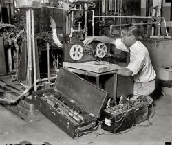 August 24, 1929. "Donald H. Brooks, Bureau of Standards." View full size. National Photo Company Collection glass negative. So -- what's he doing?
Data acquisitionMr. Brooks appears to be doing some kind of engine dyno work.  He's probably recording performance data.
The "slab" the engine/dyno is mounted on is a tee-slot base.  The tee-slots make it a nearly universal platform to work from.  The top is/was machined flat and the tee-slots added.  Lots of heavy machining goes into those things and their price reflects just that.  Sometimes you'll see them sitting on the floor (as this one) or they can be mounted flush and built-in to the floor.
One of the batteries on the floor is 6 volts.  The other one appears to be 8 volts.
What appears to be a flexible driveshaft comes off the front of the engine and (I assume) enters the back of the recorder box.  For measuring RPMs?  The recorder box almost looks like an old ticker tape machine.
The bar device in the box looks to me like some kind of an electrical shunt for measuring current, but it's a much more complicated shunt than I ever used.
The plumbing?  Part of it cools the engine that's under test.  Part of it cools the dyno brake.  The built-in complexity of the contraption might have been to make it universal?
The BoxIf you look at the box on the ground, there seems to be huge pendulums with electrical contacts on the sides.  He has that device leaning on the slab the engine is on. Then on the "recorder" device, the tape seems to go thru an arcing or vibrating styluses. My best guess is that this may be a vibration measuring device?
[The pendulum thingy looks something like a tuning fork. - Dave]
Flux Capacitor 1.0The contraption geek in me just had a stroke. So we have some great big mass of stuff on a thick concrete or forged metal slab. Some sort of inline-6 internal combustion engine. A mess of pipes and valves bordering on Three Stooges territory. I doubt the reel-to-reel is a magnetic tape recorder, since mag tape was just invented a year earlier. Or maybe it is, since it's said that the early heads were needle shaped and shredded the tape. Could it be some type of paper tape that a stylus draws on? Wish I knew what was in the big case he's leaning on. The big thingy at the left looks like the 2 counterweighted bars will vibrate at a precise rate, maybe used to calibrate something. Or maybe it's an early portable 60Hz AC inverter? I'm all atwitter.
[There were wire recorders in 1929, and devices that recorded on a thin strip of metal, but magnetic tape recorders (and magnetic tape) as we know them were still some years away. This would seem to be motion picture film. The reels are marked Eastman. Later our friend is inspecting it with a film editor. I wonder if he's using it as a kind of oscilloscope, recording a waveform or spark. Click to enlarge. - Dave]


Alumni NewsFrom the Alumni News section of Ohio State Engineer, November 1923:
CHEMICAL ENGINEERING
Donald Brooks, '21, was one of the injured in the recent explosion at the U.S. Bureau of Standards, which was fatal to some. The men were conducting experiments on an aeroplane motor when it exploded. Mr. Brooks has fully recovered from his injuries.
Film on reelsHe couldn't be recording photographically in either of the shots as the "film" (which, from the width and sprocket pattern, certainly appears to be 16mm motion picture film in form) is completely exposed to light. Note also that the visible film appears to be completely opaque, no sign of any images. Perhaps the "recording" is being done by means of perforations, embossing or etching, and film base is being used because sprocket drive would help assure consistent speed.
[If he was doing any photographic recording on motion picture film -- recording the passage of a spark between two electrodes, for example -- he could do it in the dark, or have his apparatus covered. Or maybe it's some kind of specialized film, and the spark is so much brighter than the ambient light, it doesn't make any difference. Or it might not be photographic, if the film is being inscribed with something like a needle. Or maybe you start out with exposed film and the spark blasts away the emulsion. Or maybe ... - Dave]
Mr. BrooksGentlemen, It's clearly evident here that Mr. Brooks has discombobulated the electrostratitherm drive as a precautionary measure before threading the worm gear through the tape drive. Thereby preventing any malfunction of the tapeworm as it makes its way past the geardrive. It's as plain as the nose on his face.
[Does that titanafram look loose to you? - Dave]
Frequency StandardThe cylinders on the ends of the bars are not solenoids, they're just extra masses to reduce the frequency of the device. The actual circuit is driven by making and breaking an electric circuit that is used to excite the large wire coil in between the two bars. When the circuit is made, the coil energizes and draws the two bars in together breaking the circuit again and allowing them to spring back. The two blocks further up the bars are travel limiters to ensure both arms travel the same amount.
Self sustaining frequency standards (with pickup coils and drive coils) were a long way off then, so they had to make do with make-and-break solenoid type ones instead.
My father had a smaller one of these babies back in the late seventies in his workshop. He'd salvaged it when they threw it out of the place he worked.
The longer arm meant that a heavier mass could be used for the same frequency so it would be more stable and easier to stay in calibration. The small ones had to be calibrated against the big ones which in turn were calibrated against masters held in standards labs.
[Whew. Glad we cleared that up. - Dave]
Don&#039;t Touch That DialI was thinking, perhaps he was about to throw open the switches on the sonic oscillator, and step up the reactor-power input three more triangles.
That Pendulum ThingIs probably a frequency standard. The cylinders at the near end would be solenoids that drive the tuned bars. These induce a current in an electromagnetic pickup (like a guitar pickup) and produce a very stable fixed frequency. Before fully electronic oscillators, these were widely used for precision frequency generation. The Bell system used miniatures as tone generators in the early tone-signalling system that we used to call Touch Tone. I have a couple in my junk parts bin. But those, from the 50s, are about the size of a small Sharpie.
Shorpy, home of humor and intellectHonestly, the amount of insightful posts on this site continues to blow me away. (And I'm certified hurricane-proof by the guvmint, so it's really hard to blow me away.) You have regular geniuses (said in earnest) teasing out the story behind pictures like this, and regular comedians (again, in earnest) making hilarious asides on the subject. This site, friends and neighbors, is why the Intarwebtubenets were/was/is/am invented.
Photointerpretation"My engine design is the smoothest and quietest made."
The Bureau of Standards was often involved in work for the patent office resolving patient claims and disputes, so testing parameters of an engine was not unusual for that time period. 
The box on floor left that that looks like a tuning fork, operates much like an old doorbell. The forward coil near the weights is what drives the bars movement.  The two black assemblies further up the shafts are the switches that cuts the voltage on and off to the lower coil or the electromagnet. That combination makes the two spring steel shafts oscillate back and forth and the large weights on the end limit the frequency it oscillates at to a lower speed. That assembly is powered by just one battery. It’s sole function is to “chop” or turn the DC voltage of the other battery on and off at a low fixed frequency. That chopping, turning on and off of the voltage from the other battery makes a square wave AC voltage needed to drive a transformer. In essence you could call that assembly an inverter. That principal of converting DC to AC was used up into the 1950’s and by then it was small compact unit and simply referred to as a vibrator. 
That AC from the chopper box drives a transformer and is what creates the high-voltage needed for the spark gaps on the film reel assembly. The film reels and sprockets are driven by that flexible spring steel shaft coming from the geared reducer on the end of the engine crankshaft.
In the 1920,s numerous methods were tried in an effort to make talking pictures.  One method was modulating a spark arcing on film to create or burn or gap of varying width that could be used with a light source and photocell. That test being performed in the photo is using a similar principle. Rather than modulate the voltage to the spark gap, the voltage and frequency to the gap is fixed. The speed of the film is varying giving a wider gap/burn at lower speed and narrow gap/burn at a higher speed. That will give a running record of the speed or smoothness of the engine. If the engine is rough running the gap on the film will be of varying widths. If the width of the burned gap is uniform, the engine will be smooth or quieter. That arrangement is simply recording the varying speed of the engine. 
To reinforce testing of steady speed or smoothness of engine, note he is looking at film through a magnifying lens. His interest is not the information on the film as a whole, but rather sampling short distances at different locations on the film.
By 1929 that was old technology. Government was often slow in updating their equipment.
Oh Noes!Whatever he's doing, he's just exposed the film rendering it all useless.  Oh noes!
[Read the other comments. Whether it's exposed or not wouldn't make any difference. - Dave]
Gen SetThat motor appears to be connected to a generator in back. I suspect that our intrepid researcher is measuring motor RPM against a calibrated time base to determine AC frequency.  
  We take it for granted now, but time and frequency were tough problems back in the electro-mechanical era.  Individual generating stations were alone, unless they could synchronize their output frequency to the network.  Failure to synchronize AC frequency creates heat and a loss of efficiently in transmission networks.  
Gasoline TestingGasoline quality testing measured the preignition of gasoline using this machine called an Octane Engine.  Lower quality gasoline causes preignition, or "engine knock," which is measured by the vibration in the test engine.  The less the engine vibrates, the higher the Octane value.  Gasoline is still measured and rated in this manner today, but using a more modern engine.
It&#039;s obvious.His magnetic flux capacitor is being calibrated by the retroencabulator.
But the 16mm film seems to be what we used to call "full-coat" -- coated with magnetic oxide from edge to edge for sound recording.
Testing engine power at varying humidity levelsThe tape is paper. The apparatus on the left generates a high voltage spark which periodically burns holes in the paper tape. It was a brand new design in 1928 according to the NBS.
All the pipes were used to mix steam into air to get a fixed humidity for each engine test, and spark advance was changed to optimize power. Tests were at 500 rpm full throttle on a 6 cylinder ohv engine.
The resulting engineering report is available free via Google by search results "donald brooks national bureau of standards june 1929".
Earlier spark accelerometers were used by GM for fuel economy testing by fifth wheel:
https://blog.hemmings.com/index.php/2010/05/24/proven-practices/
Brooks' work was referenced right into the 1950s, and a glance at his papers shows he was a pretty technical fellow; i.e. there's a lot of advanced mathematics.
(Technology, The Gallery, Natl Photo)