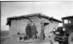 Lurtie Jay, George Phillips, and Ernest Ireton standing in front of a sod house.  The license plate appears to read 1929 but the photo is dated 1927 on the reverse.  The group was likely in the Alliance area of Cherry County, Nebraska.