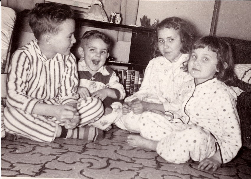 "If you don't go to sleep, Santa Clause cannot come," is what our mother said every Christmas Eve until we were old enough to know otherwise. Here in this photo, "otherwise" is becoming the reality for me. I'm the little girl and my older brother has just told me "Mom IS Santa Claus". My sister's face betrays her emotion as she thinks "as soon as that shutter clicks I am going to rip his head off." She did too. There was a big scene with Mother yelling "you didn't have to tell her!", which pretty much sealed the deal for me--no Santa Claus. 

Little brother is joyous. He does not know what was said, but he hears "Santa Clause." "Yay!" He will fall asleep as soon as the shutter clicks. Photo taken in the living room of our apartment in a small town in northern Minnesota. I'm 4, sister is 9, brother is 2 and the traitor is 6. View full size.