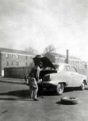 This photo, taken by my mother in 1951, shows my father with his first car: a 1950 Studebaker Champion 4 door sedan. He dated my mother in that car. They were married in October 1951, and he traded that car in on a 1952 Commander in the spring of '52. So they only had this car as newlyweds.
The reason my father bought a Studebaker was that he had come from New York City where nobody in his family had ever owned a car, or even had a license to drive one. The Studebaker dealer offered to give him driving lessons, and take him to the DMV to get a license, included in the price of that car. So a sale was made. By all reports the car was a dog - under-powered and under-braked, which is why he did not keep it long. It had a manual transmission, and if anyone ever waxed it, there is no evidence of that in this shot.
Buildings in the background are the New Brunswick New Jersey garden apartments where they lived until 1953. 
(ShorpyBlog, Member Gallery)
