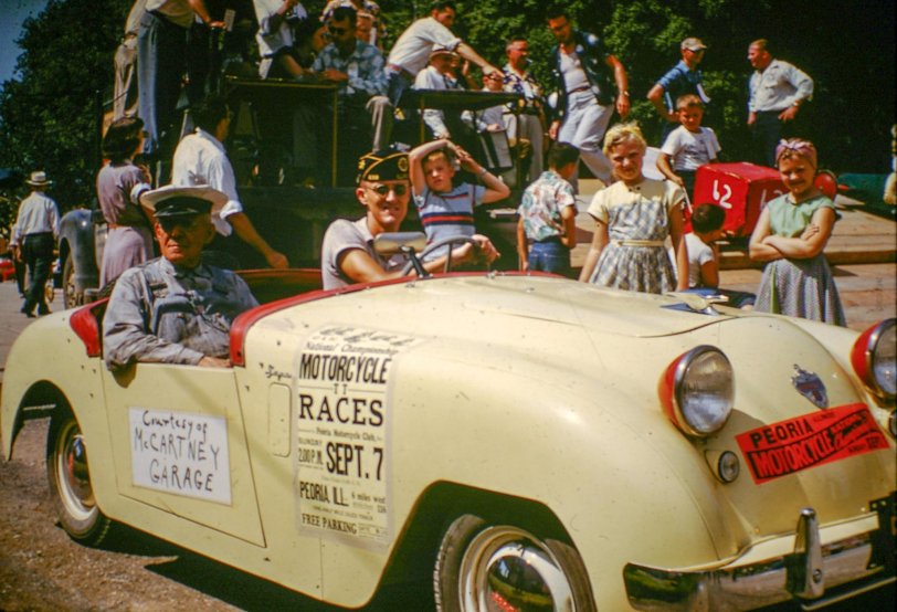 The Derby Grand Marshal riding in the McCartney Garage convertible at the 1952 Soap Box Derby 1952 in Elmwood, Illinois.
__________________
Massey Wins "Rocket Derby" as 78 Entrants Vie for Prizes
Robert Massey of Muscatine, Iowa, driving car number 71, won first Place in the A division of the 1952 "Rocket Derby," held Saturday, September 6 in Elmwood.
Massey's time for the course averaged 25.8 seconds. Second place went to Ronald Brisker of Bushnell in car number 19 while the 3rd place trophy was won by Dean Vance, son of Mr, and Mrs. Cornelius Vance of Elmwood, driving car 98. Dean was one of the most consistent drivers of the day, going down the hill four times in 26.3 seconds and twice in 26.5. There were 52 cars which ran in the A division and 26 cars in the B division. Three cars entered earlier in the A division did not run.
Cars in the A group finished in this order: 71, 19, 98. 52, 3 and 15 tie. 83, 1-17-29-55-60-88 tie, 22, 61, 13-16-45-81, tie, 11-14-41-43-91 tie, 56, 74-87 tie, 10-30 tie, 39, 12, 5, 21-25 tie. 44-78 tie, 92, 20-82-100 tie. 53, 35, 48, 64, 24, 46-57 tie, 7, 8. 33, 62, 49. Average times ranged from 25.8 seconds to 30 seconds. 
Competing against 25 other entrants in the B division, Ronnie Ecklund. son of Mr. and Mrs. A. W. Ecklund of Elmwood, drove car 47 to first place in this group, with George Shaheen, son of Mr. and Mrs. Louis Shaheen of Elmwood, winning second place. Ronnie's average time was 35.55 while Shaheen's time was 36.35. Shaheen made one run of 34.2 for the fastest time of the day.
