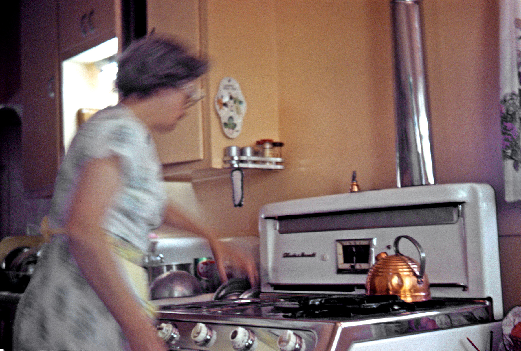 July 1964. My mother is a blur of activity in this available light Kodachrome; judging from the grates piled up on the right front burner, she's cleaning the O'Keefe & Merritt's chrome top. View full size.