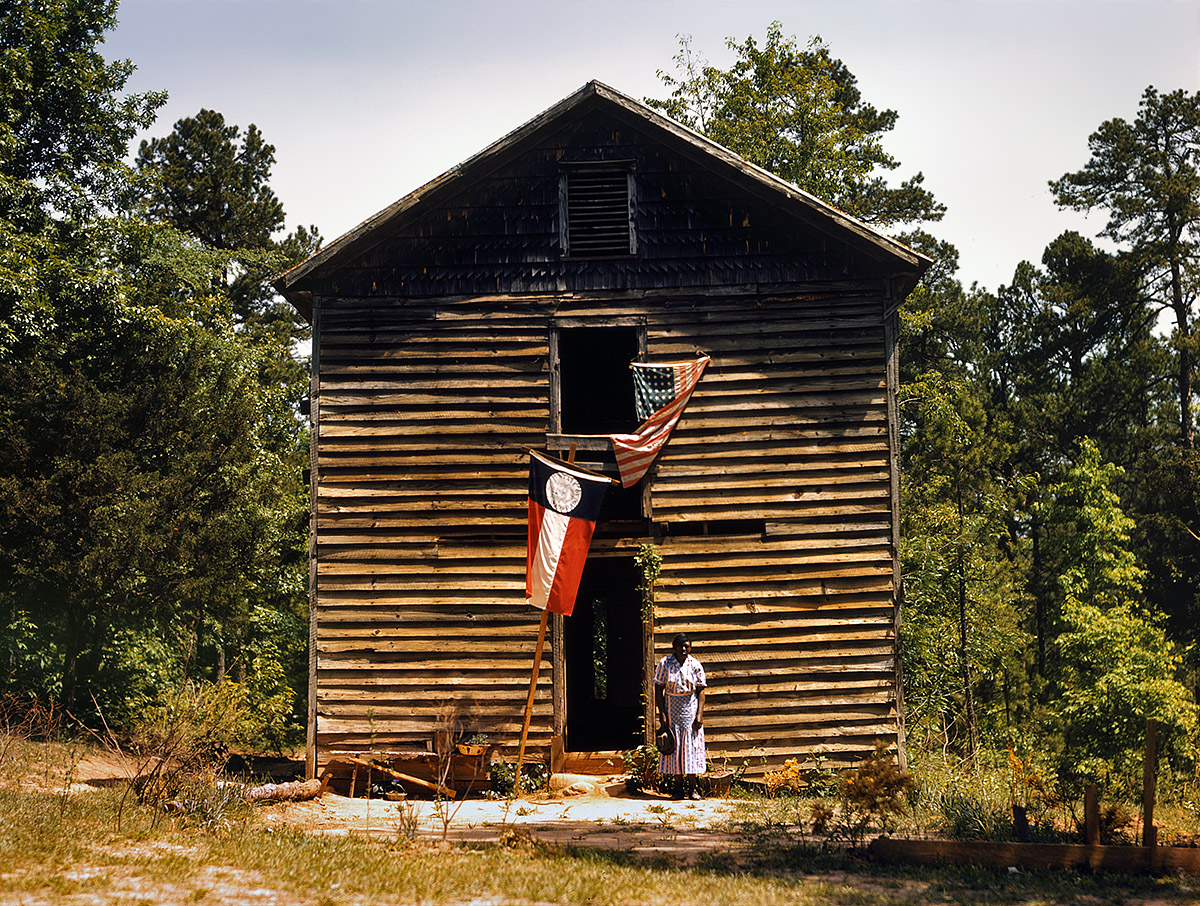 The caption for this 4x5 Kodachrome transparency is "Near White Plains, Georgia?" The circa 1941 photo, of a woman in front of a frame building flying the U.S. and Georgia colors, is attributed to Jack Delano although it bears the notation "Possibly photographed by Marion Post Wolcott." View full size.