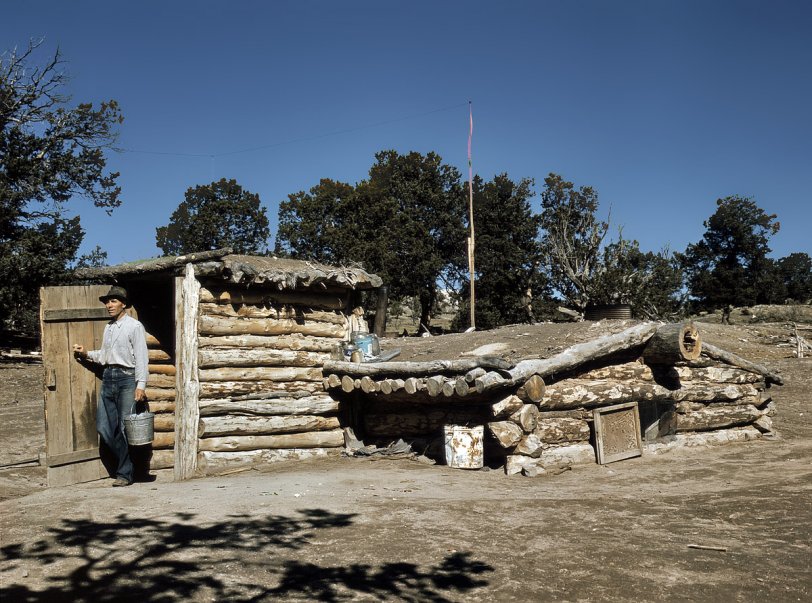 October 1940. "Mr. Leatherman, homesteader, coming out of his dugout home at Pie Town, New Mexico." View full size. 4x5 Kodachrome transparency by Russell Lee. Another example of the dugout-style structure used for the homesteader dwellings and church in the Dead Ox Flat photos. Before industry and technology gave us sawmills and frame houses, this is how the average person lived in much of the world. The dugout or pit house, with sod roof, log walls and earthen floor, is among the most ancient of human dwellings -- at some point in history your ancestors lived in one. Especially popular among 19th-century settlers in the Great Plains and deserts of the West and Southwest, where trees and other building materials were scarce, dugouts were warmer in winter and cooler in summer than above-ground structures; just about anywhere in North America the ground temperature three feet down is 55 degrees regardless of the season. [Addendum: This picture was taken using Kodachrome sheet film (5 inches by 4 inches) and (probably) a Graflex Speed Graphic press camera. The image you see here was scanned from the positive transparency itself, not a print.]
