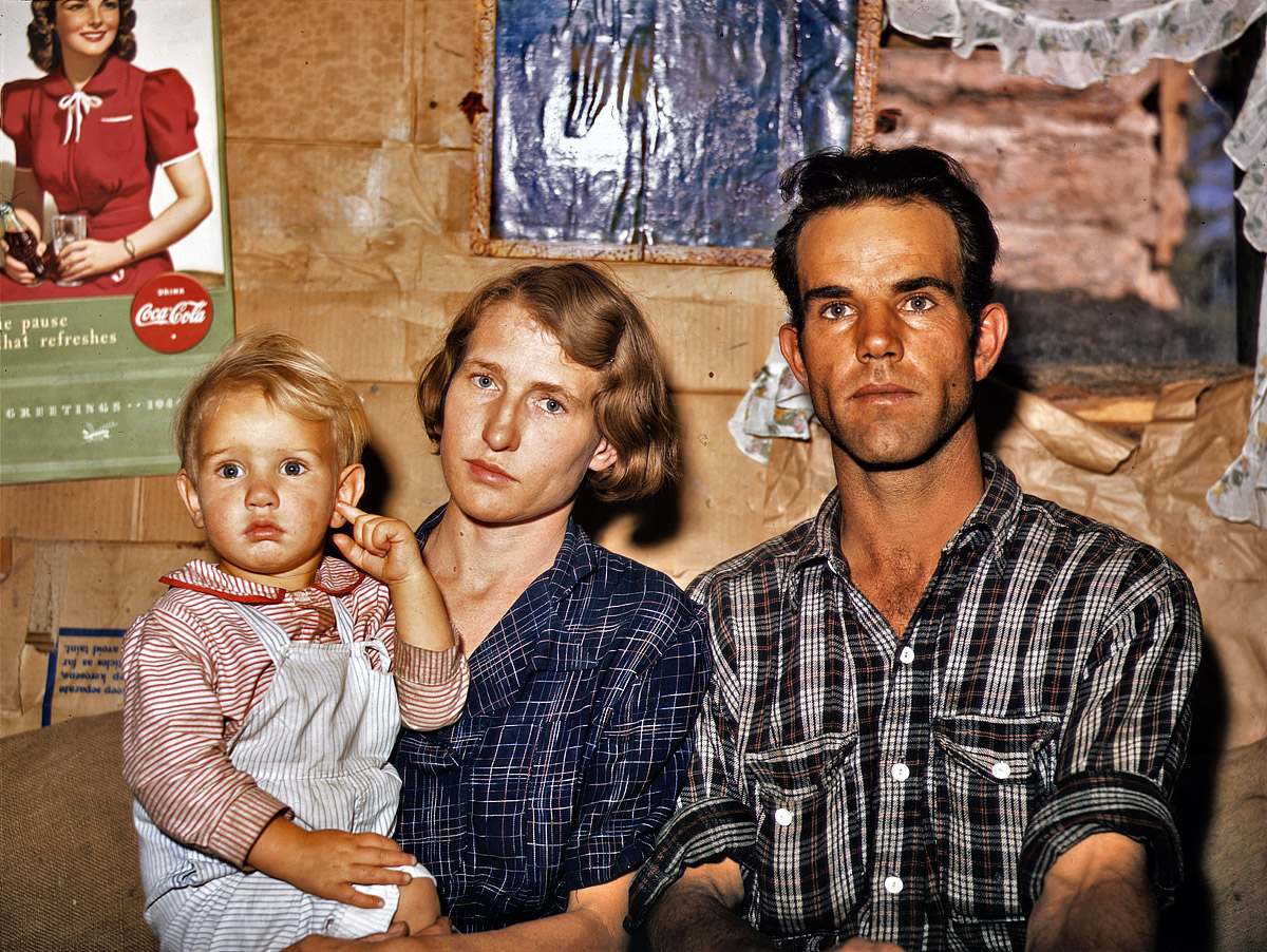 September 1940. Jack Whinery, Pie Town, New Mexico, homesteader, with his wife and the youngest of his five children in their dirt-floor dugout home. Whinery homesteaded with no cash less than a year ago and does not have much equipment; consequently he and his family farm the slow, hard way, by hand. Main window of their dugout was made from the windshield of the worn-out car which brought this family to Pie Town from West Texas. 4x5 Kodachrome transparency by Russell Lee, Farm Security Administration. View full size.