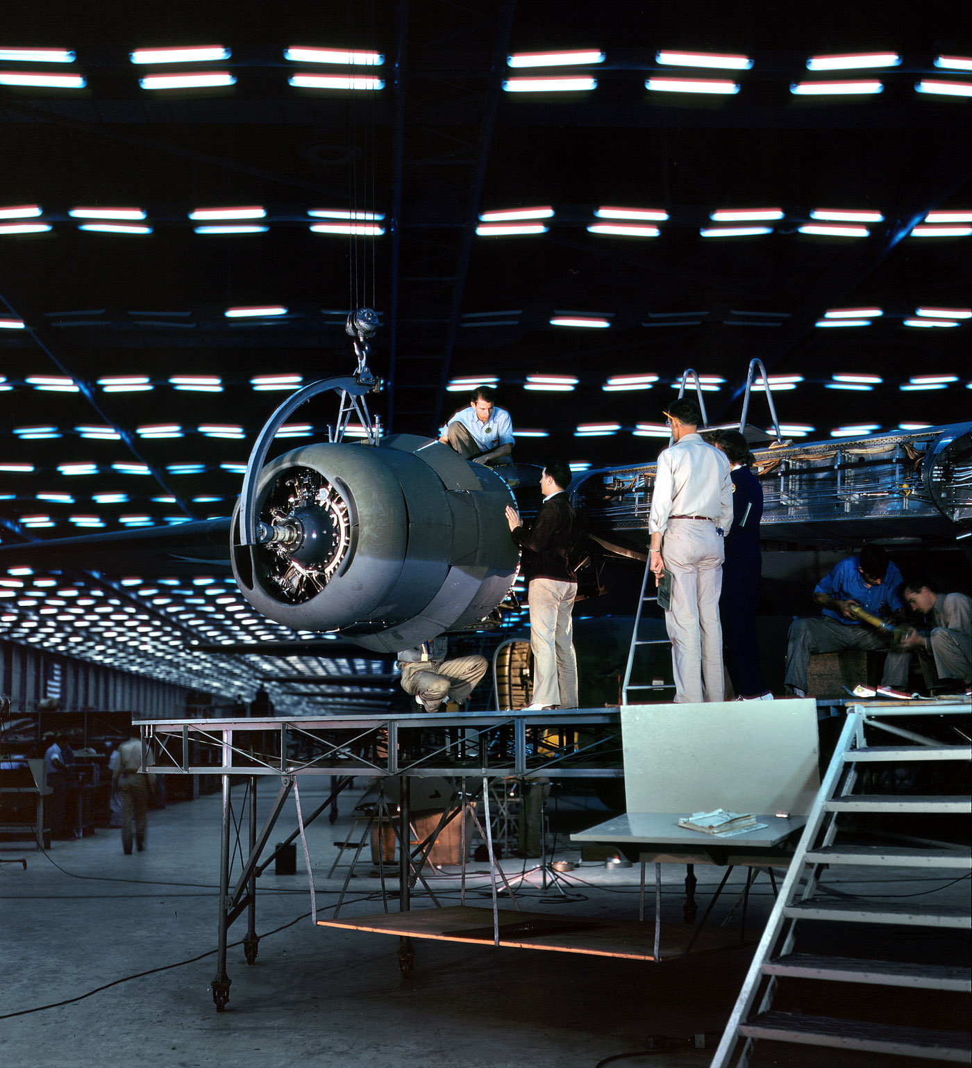 October 1942. Transport assembly hall at the Consolidated Aircraft Corporation plant in Fort Worth, Texas. Lowering an engine into place. View full size. 4x5 Kodachrome transparency by Howard Hollem for the Office of War Information.