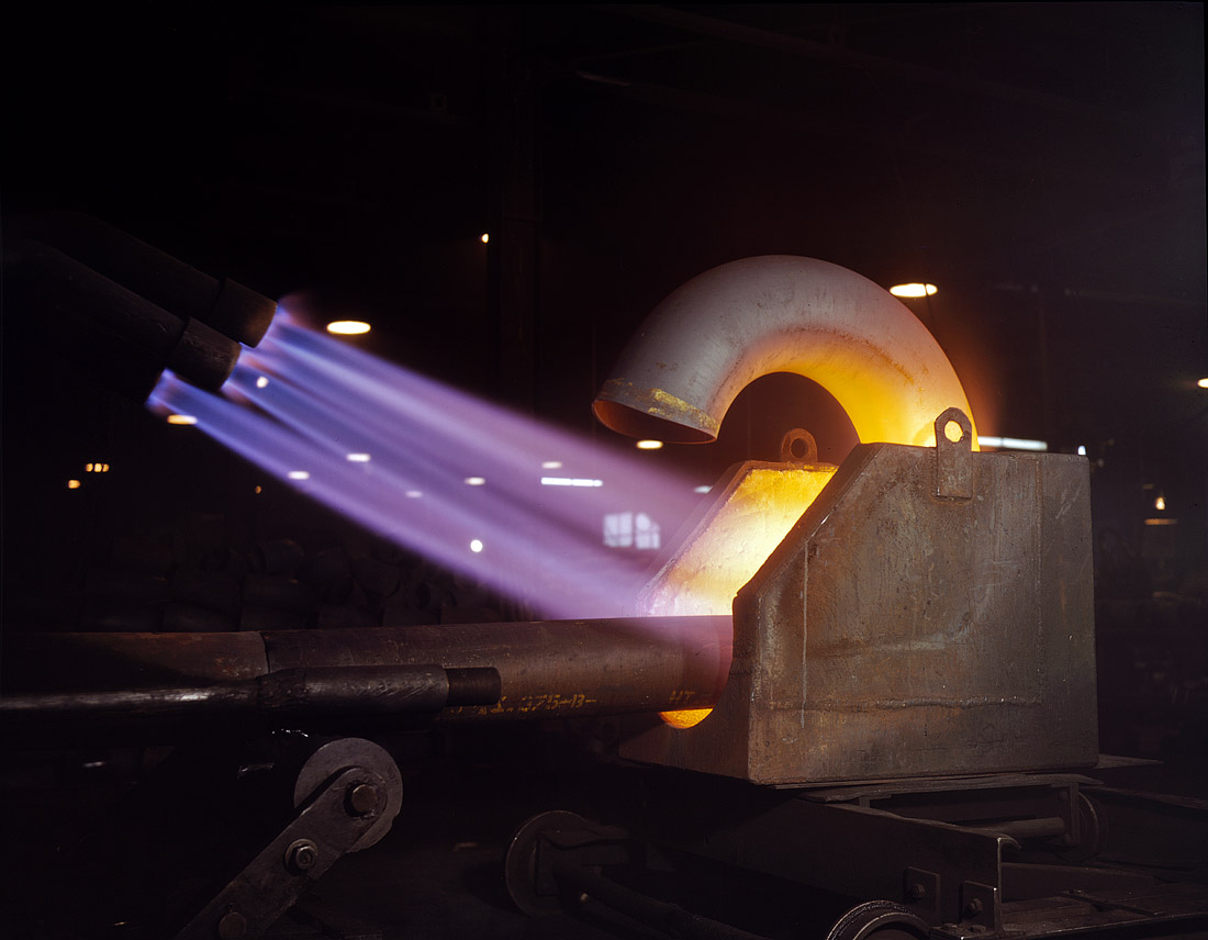 January 1942. Louisville, Kentucky. "Large pipe elbows for the Army are formed at Tube Turns Inc., by heating lengths of pipe with gas flames and forcing them around a die." 4x5 Kodachrome transparency by Alfred Palmer. View full size.