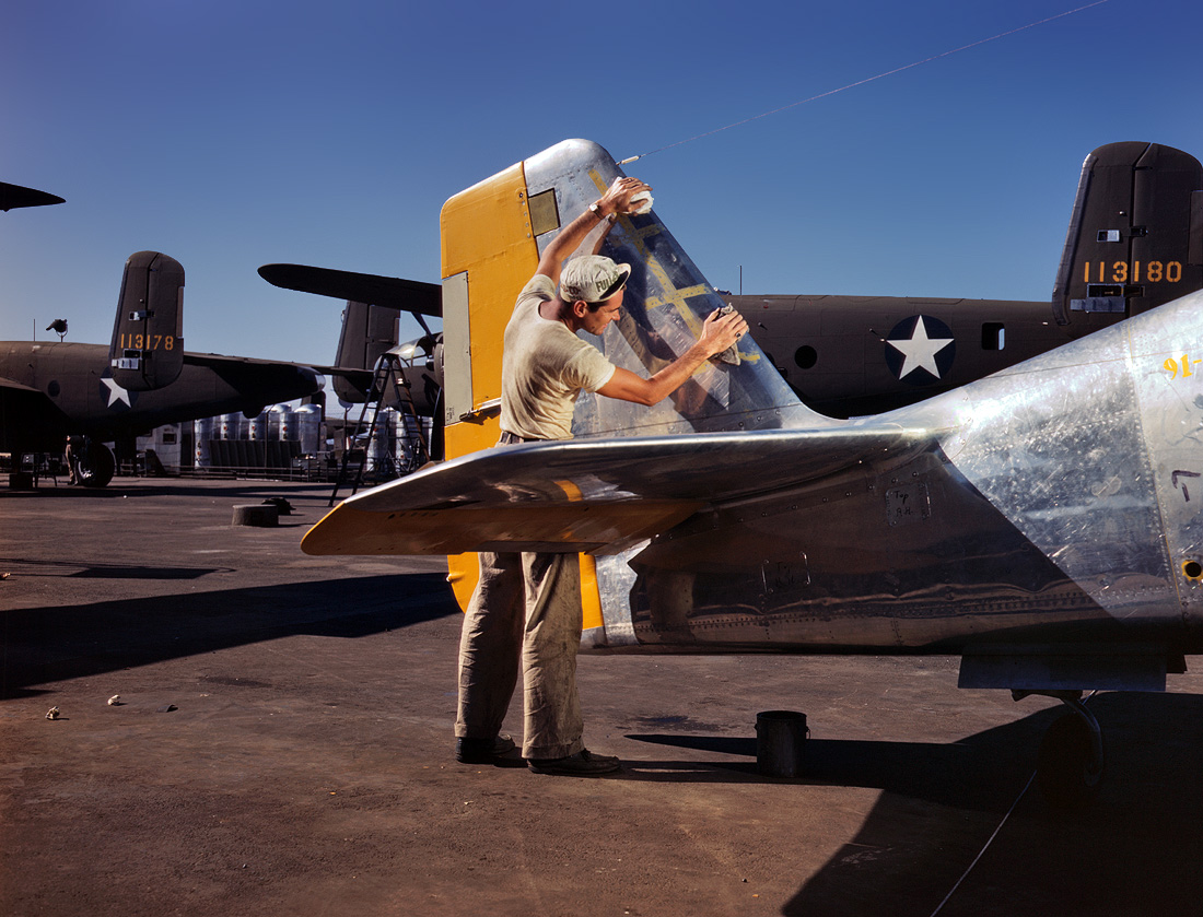 October 1942. A painter cleans the tail section of a P-51 Mustang fighter prior to spraying with olive-drab camouflage. North American Aviation plant, Inglewood, California. View full size. 4x5 Kodachrome transparency by Alfred Palmer.