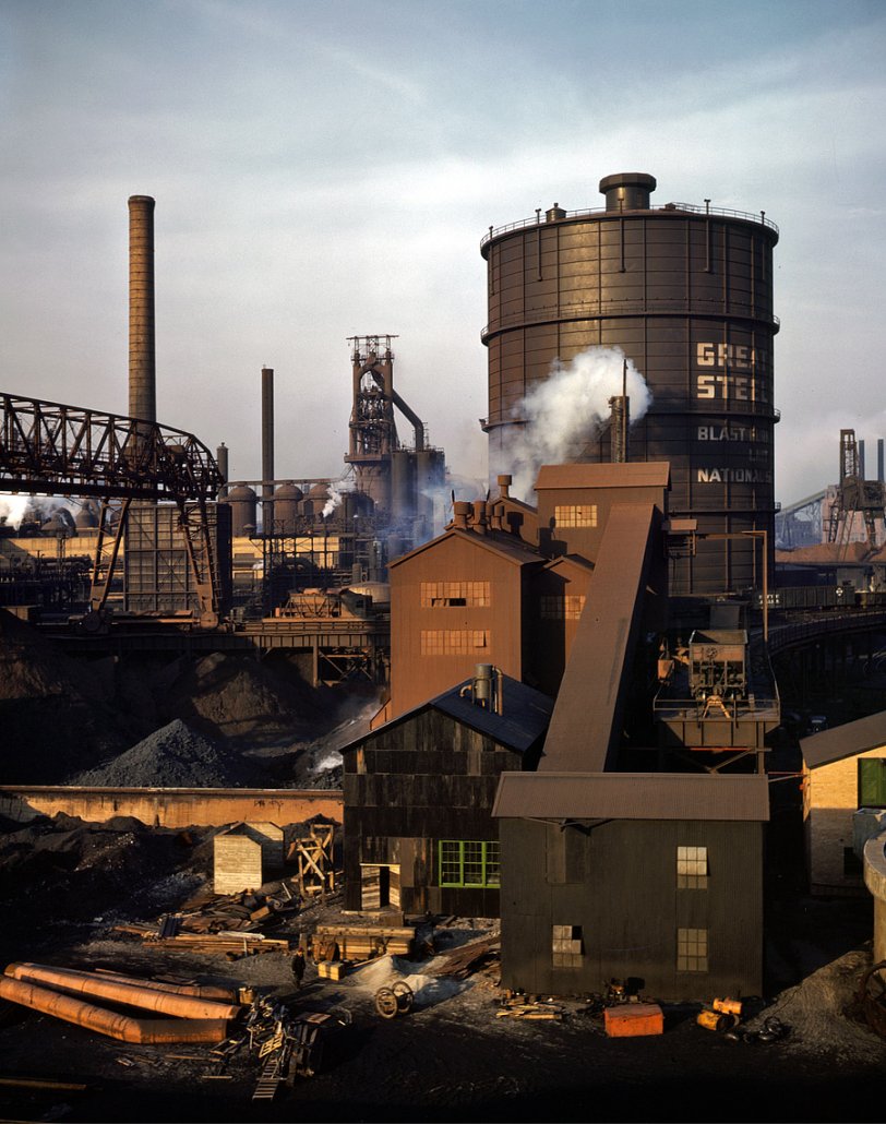 November 1942. Hanna furnaces of the Great Lakes Steel Corporation, Detroit. General view showing tank which stores gas from the coke oven. Square building and extension in middle ground is where coal is fed to a feeder belt and then transferred to a storage place on top of the coke oven. The coal is then dropped into three inverted bottle-like containers and from there fed directly into the coke ovens. View full size. 4x5 Kodachrome transparency by Arthur Siegel.