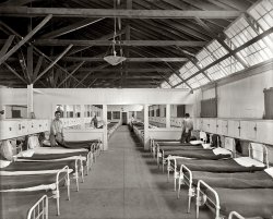 Fairfax County, Virginia, circa 1911. "Occoquan Work House, sleeping area." Part of the jail operated by the District of Columbia Department of Corrections, shown shortly after its construction. Harris &amp; Ewing glass negative. View full size.
Then and NowThe prison was closed down the 1990s, and the low security dorm shown in this photo has been converted into an center for the arts and a museum -- quite a change! 
http://workhousemuseums.org/
Love the track lightingI think it fits the decor.
The exteriorof another part of this charming facility. Click to embiggen.
"Occoquan Work House, exterior." (Harris &amp; Ewing)

The beds don&#039;t look too comfybut it's clean, there's heat and lots of natural light. I can think of worse places to be locked up. I'm guessing these guys were minimum security types.
The well-read inmateAt least one inmate here reads the Washington Post. Today the workhouse is an arts center:
http://www.workhousearts.org/
The Work HouseWhat exactly was a Work House? Sounds like something out of Charles Dickens.
I worked there.I was employed by the Department of Corrections for over ten years starting 1971.  The workhouse, at least in those days, was simply the minimum security facility of Lorton Reformatory. The DCDC had five facilities in Lorton, Virginia.
Maximum Security (the Wall, where I ate lunch every day for a dollar), Big Lorton (Central Facilities), the Workhouse (or Occoquan - never actually called Minimum Security). 
There was also YC1 and YC2, both Youth Centers. I started as a Correctional Office at YC2, then worked in the Industries Division at Central for 10 years. Many a time I have walked the sweltering underground tunnels connecting YC2 to the steam plant at Occoquan.
Occoquan was where an inmate could hope to graduate to, from Big Lorton, when nearing his parole and escape risk was very low. Inmates at the workhouse could be truck drivers' helpers, or any number of jobs at the facilities, and earned a small salary which would help a lot when paroled.
I could write a book about all that went on in Lorton, and am always thrilled to see old photos. 
Here is one of One Tower and the Salleyport at the Wall.  It was never called the Citadel.
Really this is is exterior view of same building?The interior view seems to be of a much wider building.  For instance there seems to be space for 4 rows of beds with additional room for 2 wide corridors, one in each of the bays.  Also the windows in the interior view seem to start at least 10 or maybe even 11 feet above the floor.
[As noted in the captions, the interior shot shows the workhouse dormitory and the outdoor shot shows the workhouse. - Dave]
Outdoor &amp; Indoor Shots?The more I look at the two photos, the more i think they are two separate buildings. The interior space, height of the windows from the floor ...
[As noted in the captions, the interior shot shows the workhouse dormitory and the outdoor shot shows the workhouse. - Dave]
More elevated steamAnother photo showing radiators 5 feet or more off the floor.  First time I saw this was from another Shorpy picture of an auto repair shop. Only times I have ever seen this.
SimilarThis shot reminds me a lot of these Civil War images.  Aside from steam radiators and electric lights, there's not much difference.
https://www.shorpy.com/node/2388?size=_original
https://www.shorpy.com/node/2384?size=_original
Been there, done thatSpent two nights there with Mr. Chomsky and Mr. Mailer back in '67. Good place to plan the Revolution.
(The Gallery, Harris + Ewing)